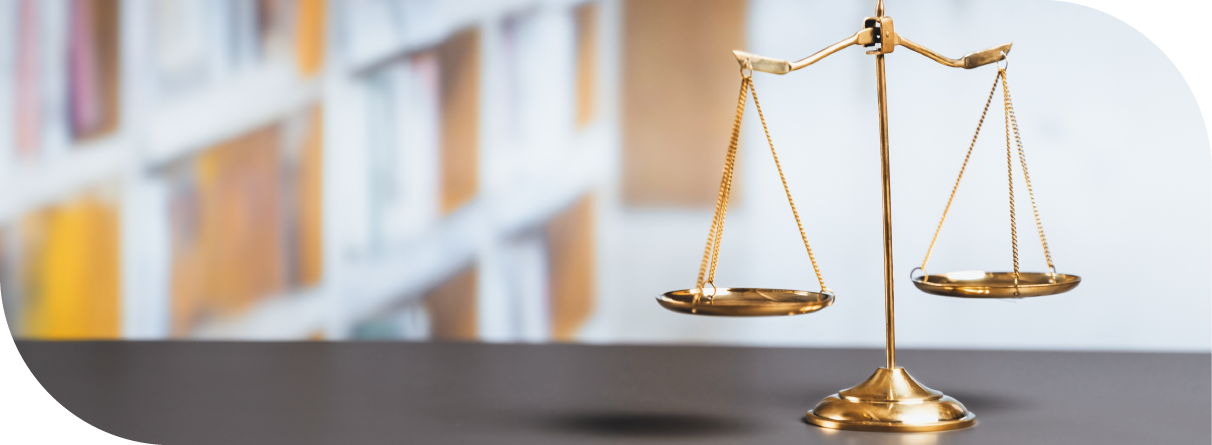 Golden balance scale on a dark surface with blurred bookshelf background, symbolising fairness.