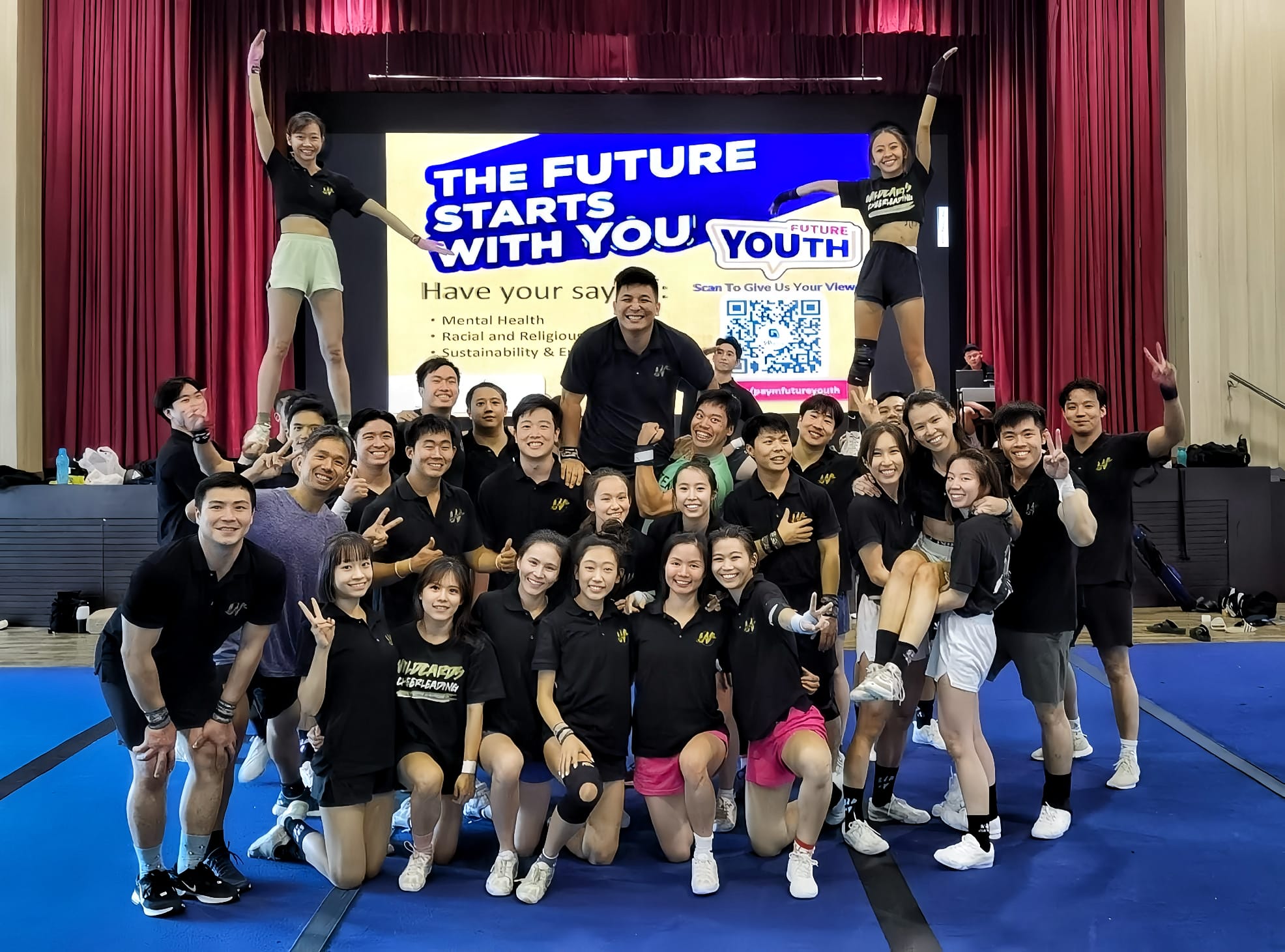 A large group of people in matching black shirts gather in front of a stage displaying the text "The Future Starts With You".