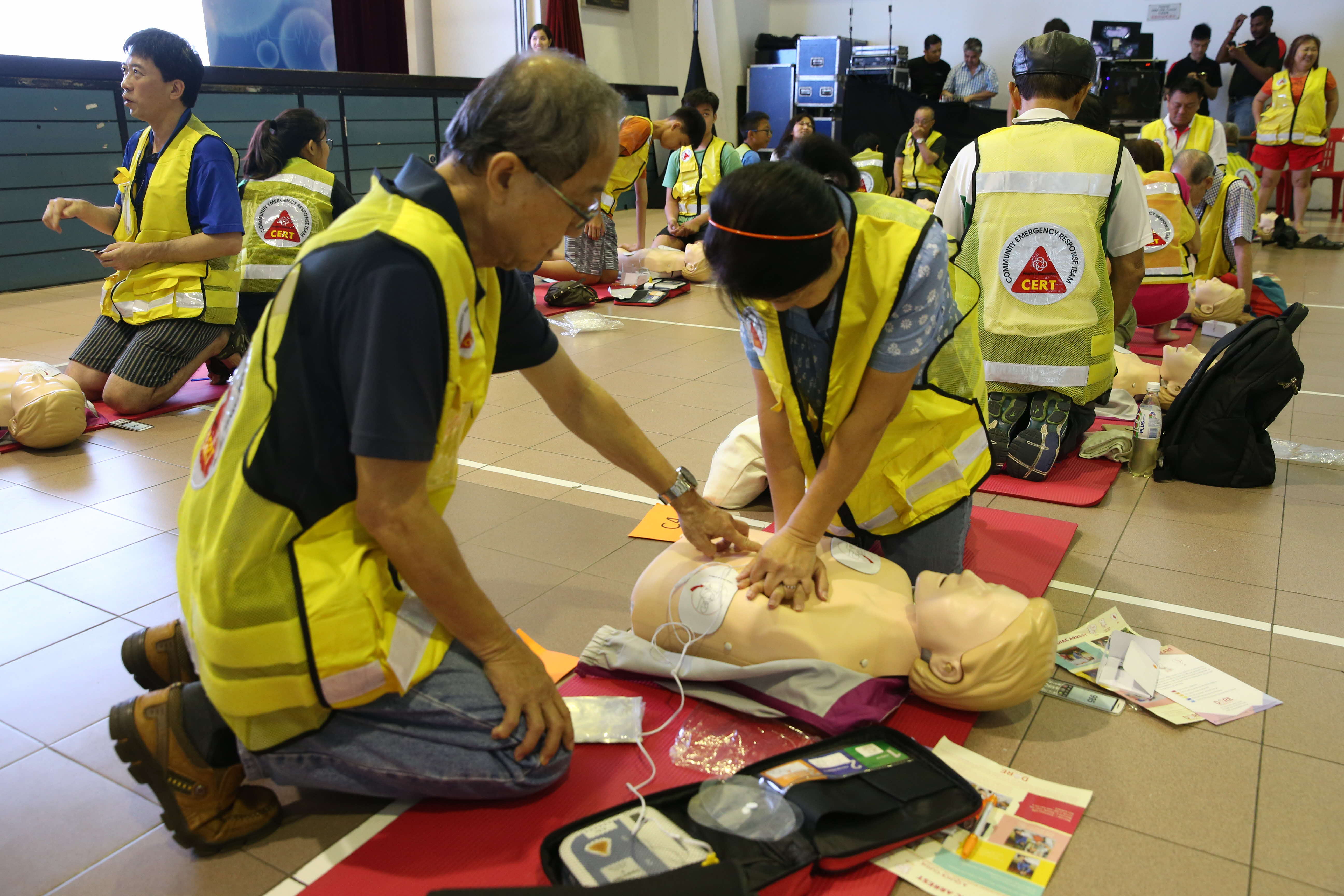 People in yellow vests practice CPR on mannequins in an indoor training session.