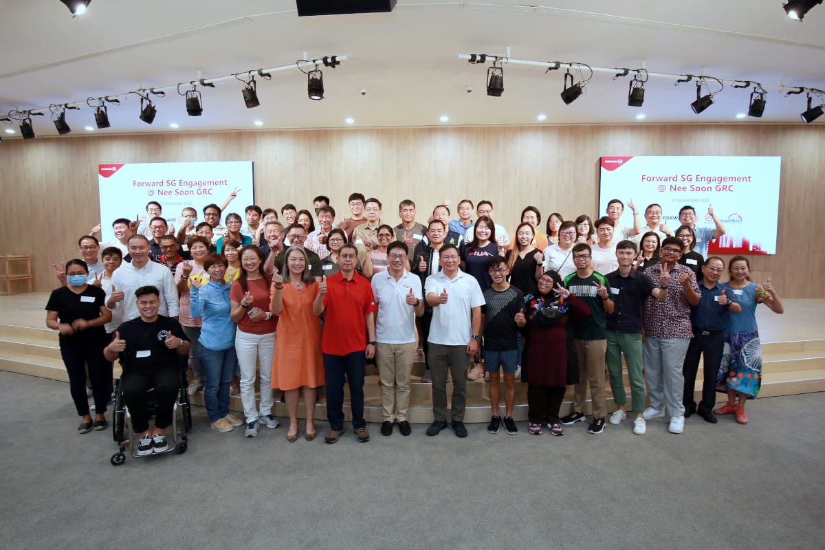 A large group of people standing on stage, giving thumbs up, with two screens showing "Forward SG Engagement @ Nee Soon GRC."