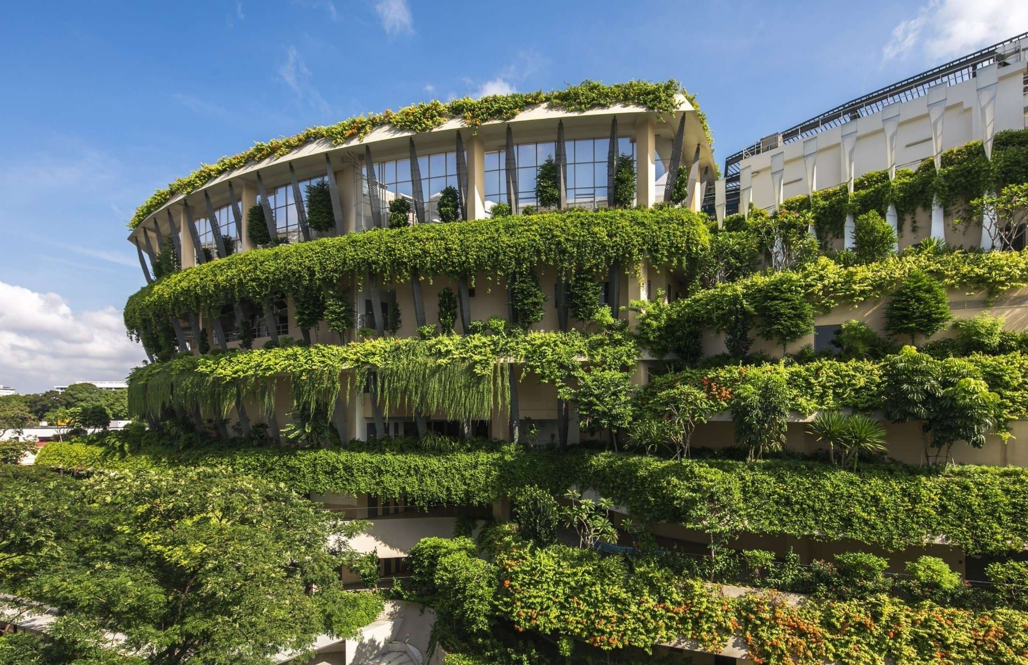 A large, multi-story building covered with lush, green vegetation on all levels against a backdrop of blue sky.