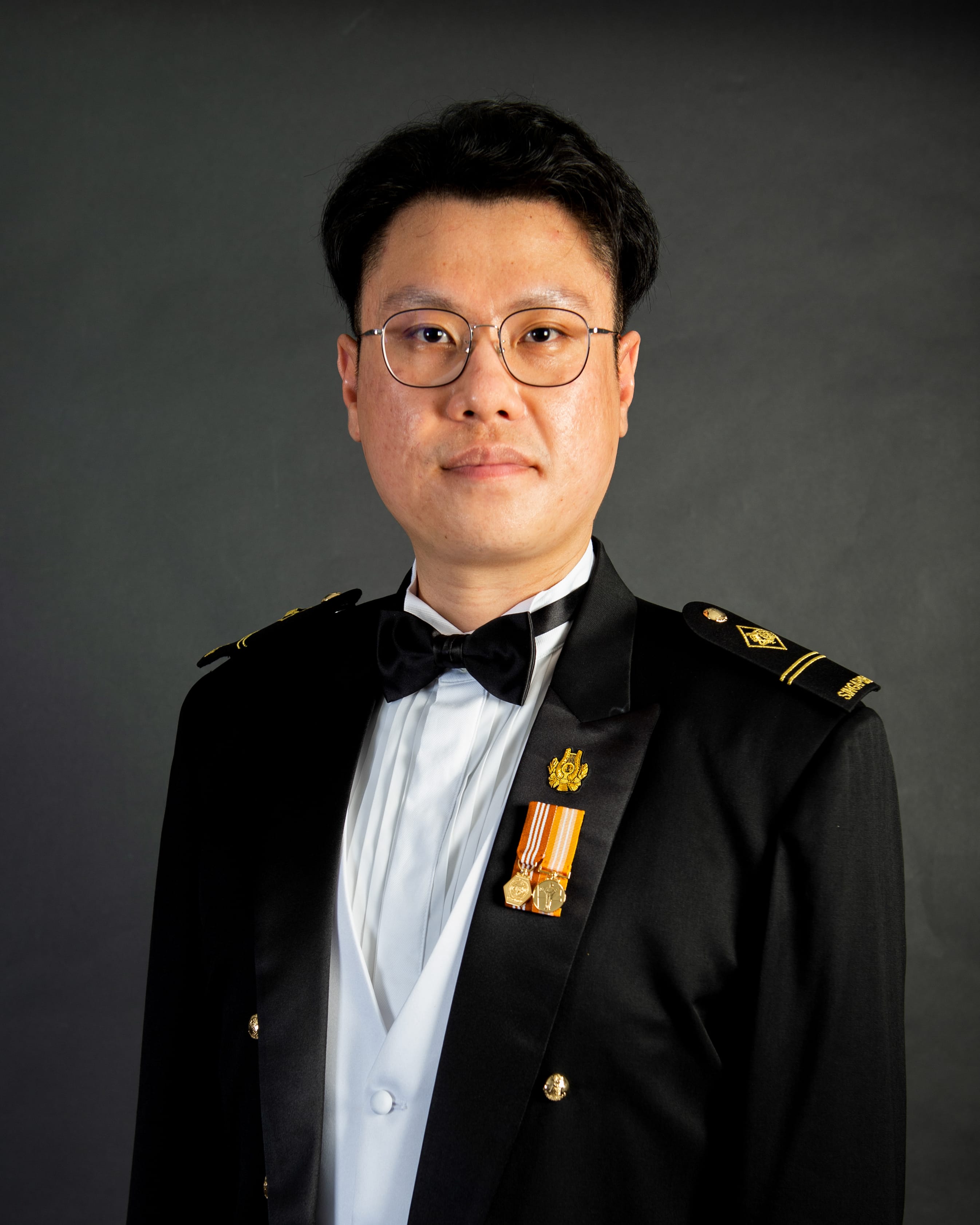 ME2 Dax in formal SAF mess dress uniform with medals and glasses against dark background.