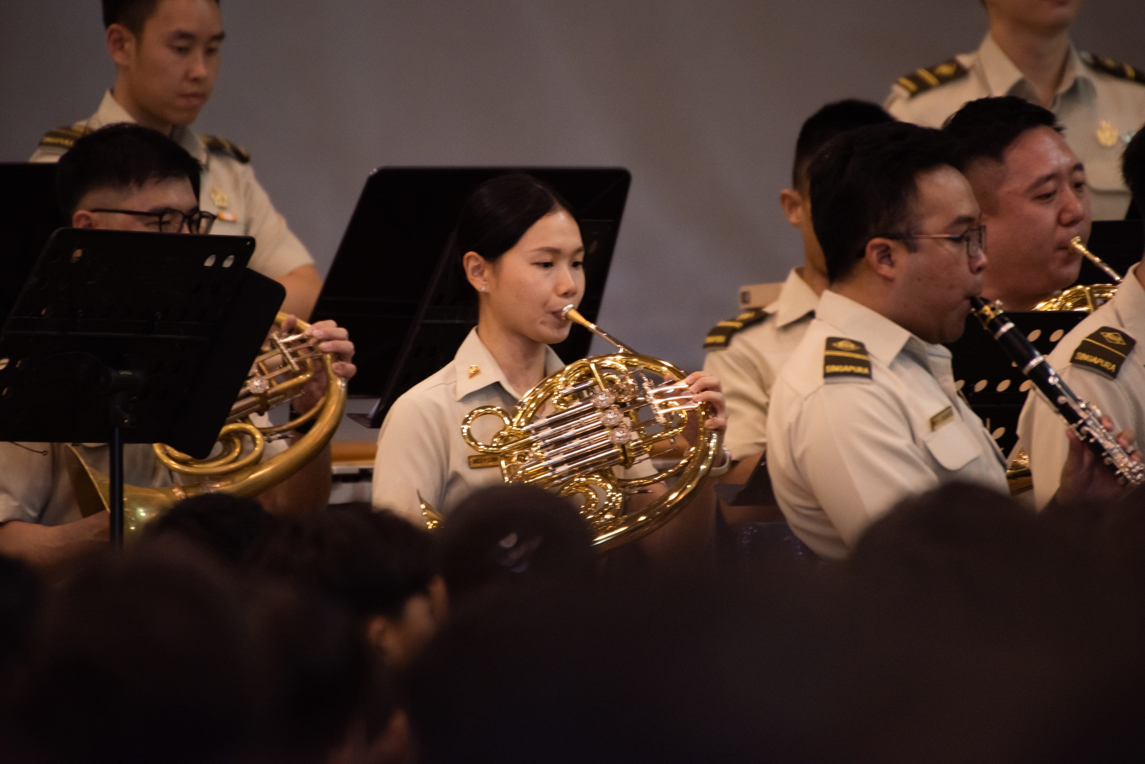 Female French horn player in uniform performing with band during a live music ensemble.