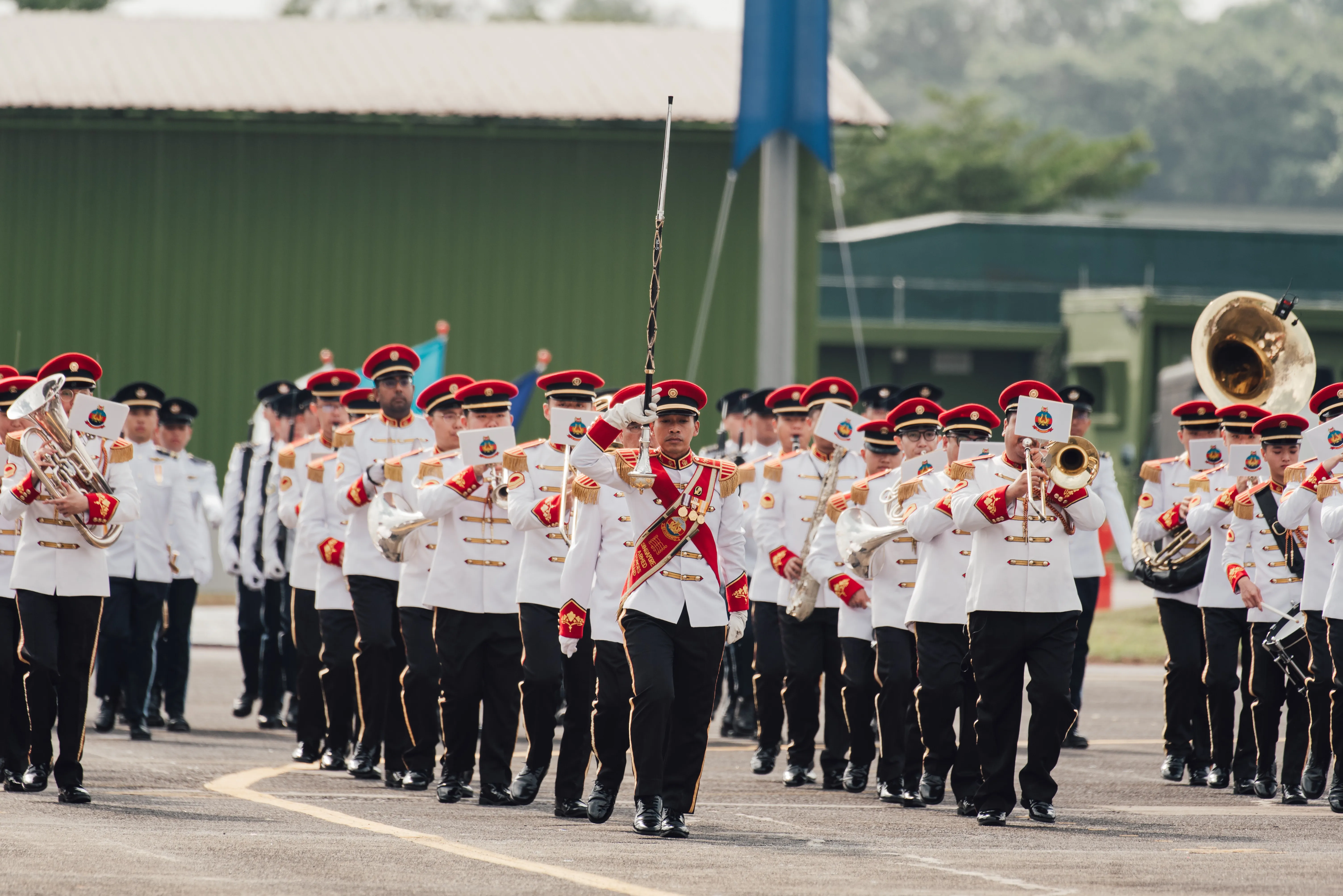 SAF Band marching in ceremonial parade, led by conductor with baton and brass musicians