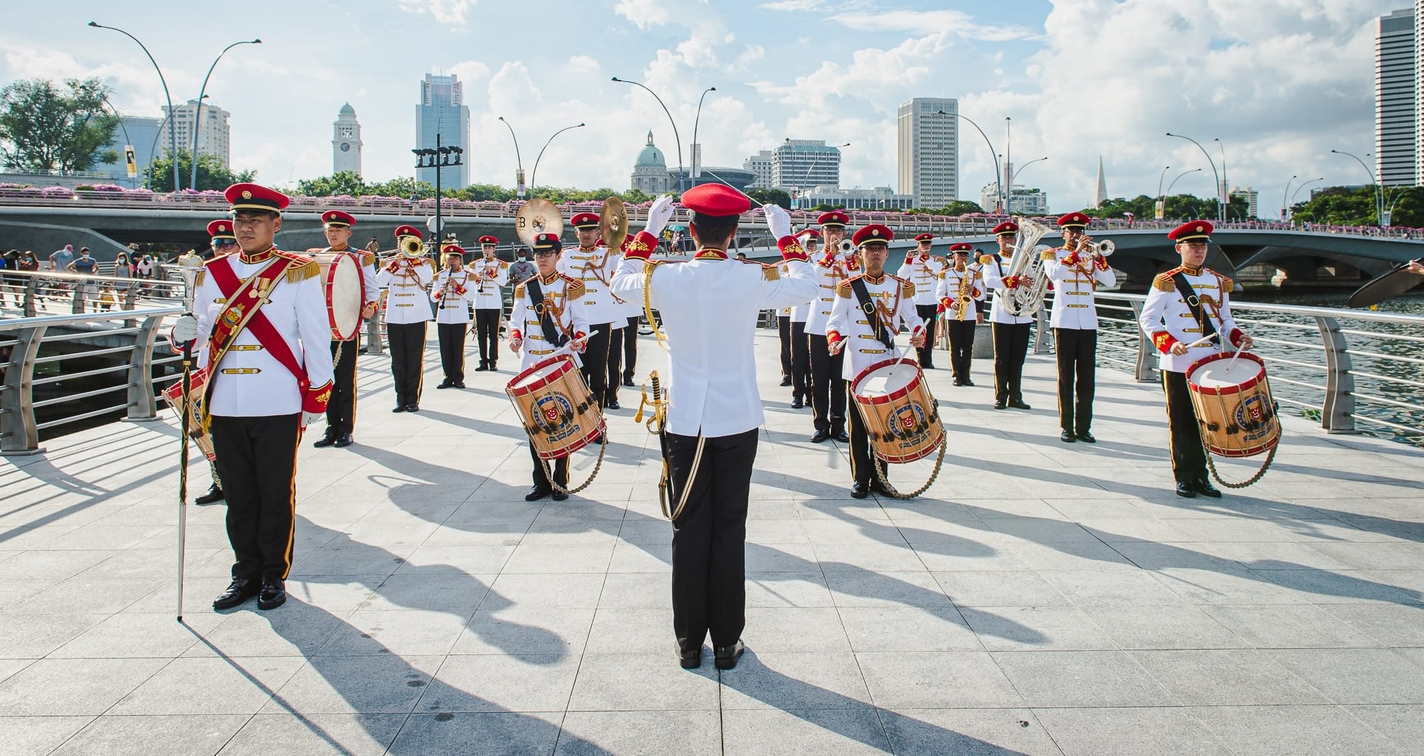 SAF Band performs outdoors in ceremonial uniform near Marina Bay with a conductor in front.