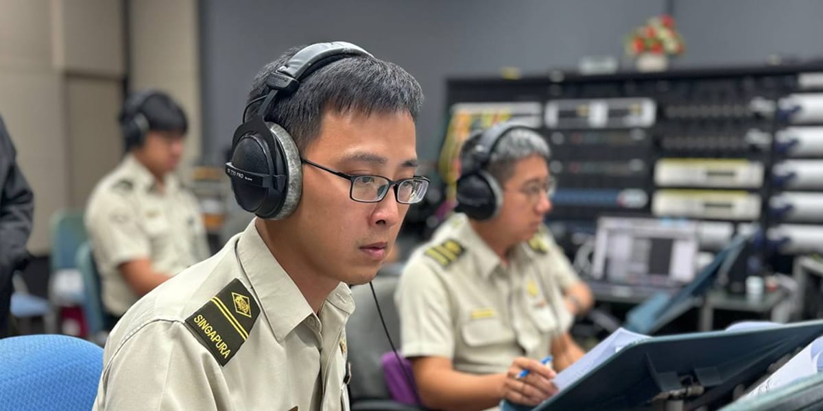 Musicians in uniform with headphones follow scores during a rehearsal in a studio.