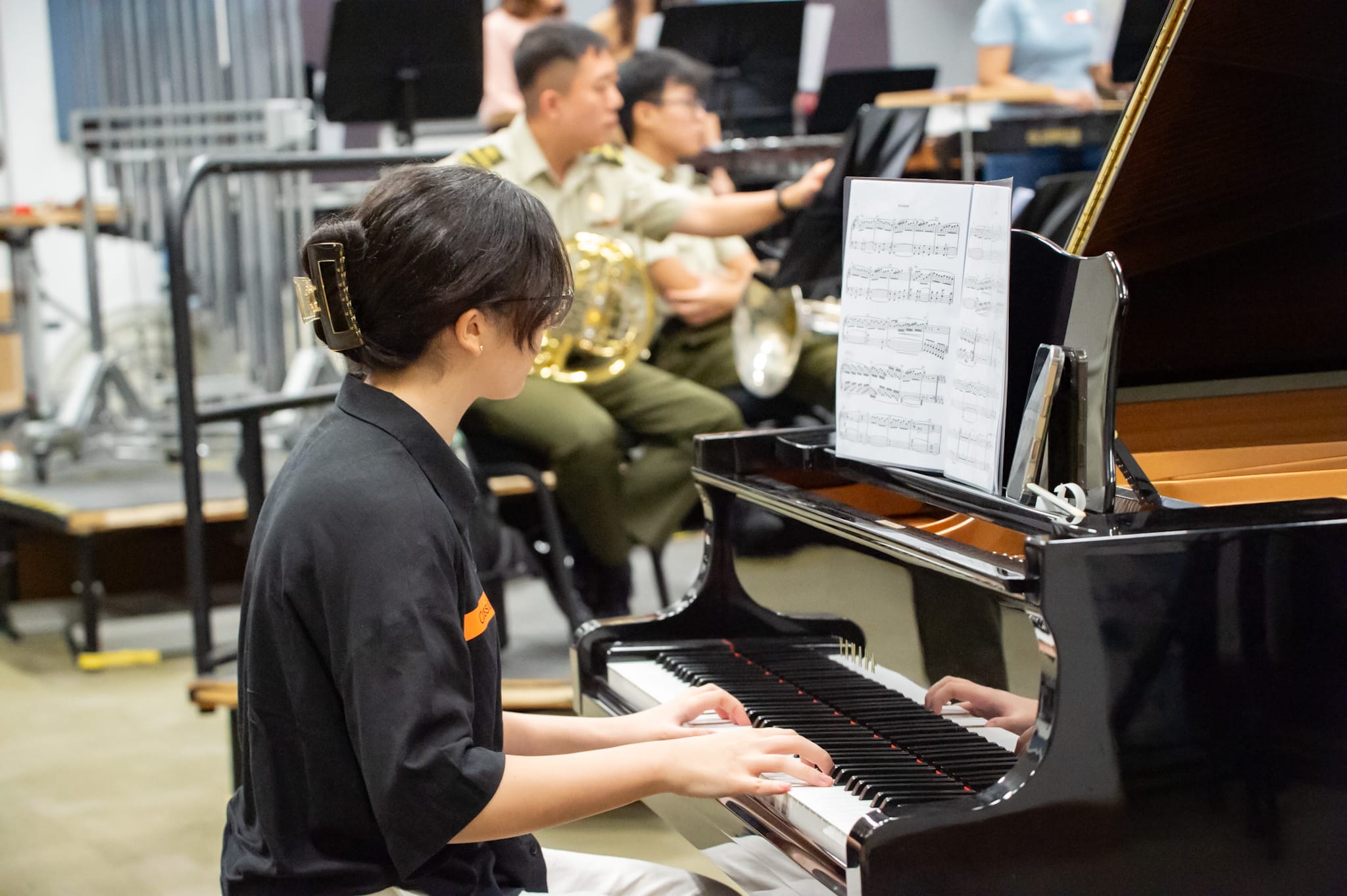 A pianist playing during a military band rehearsal while others play behind.