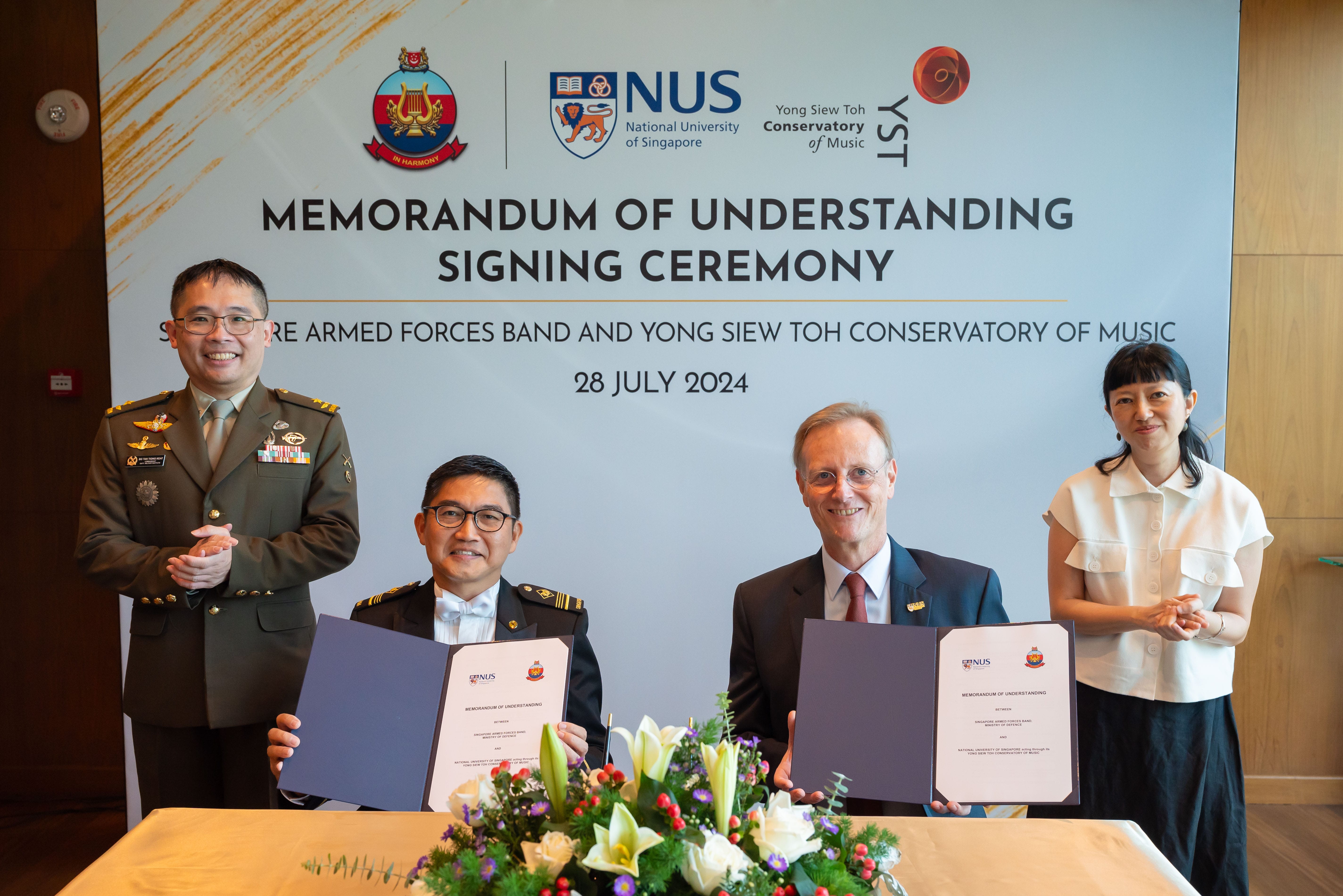 Representatives from SAF Band and YST Conservatory holding signed MOU folders at ceremony table.