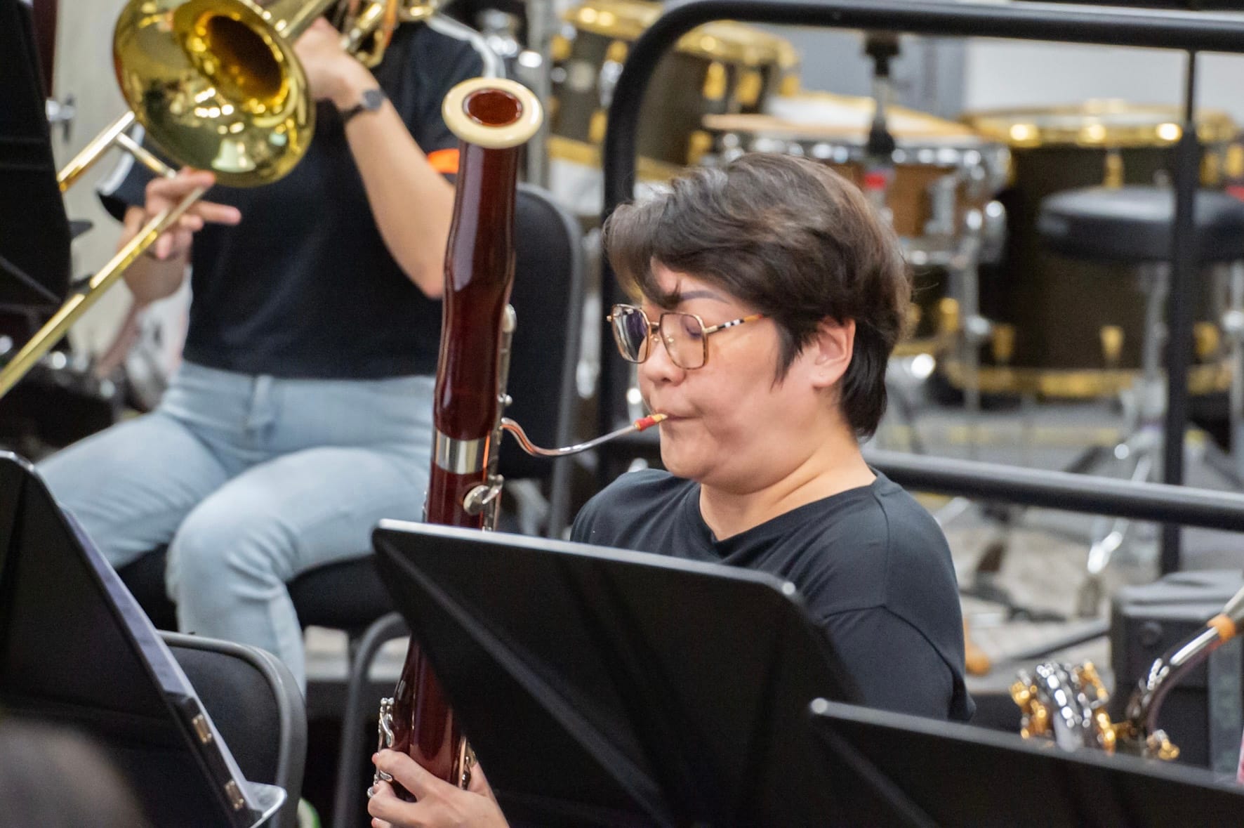 Musician playing the bassoon while other brass players are in the background during practice.