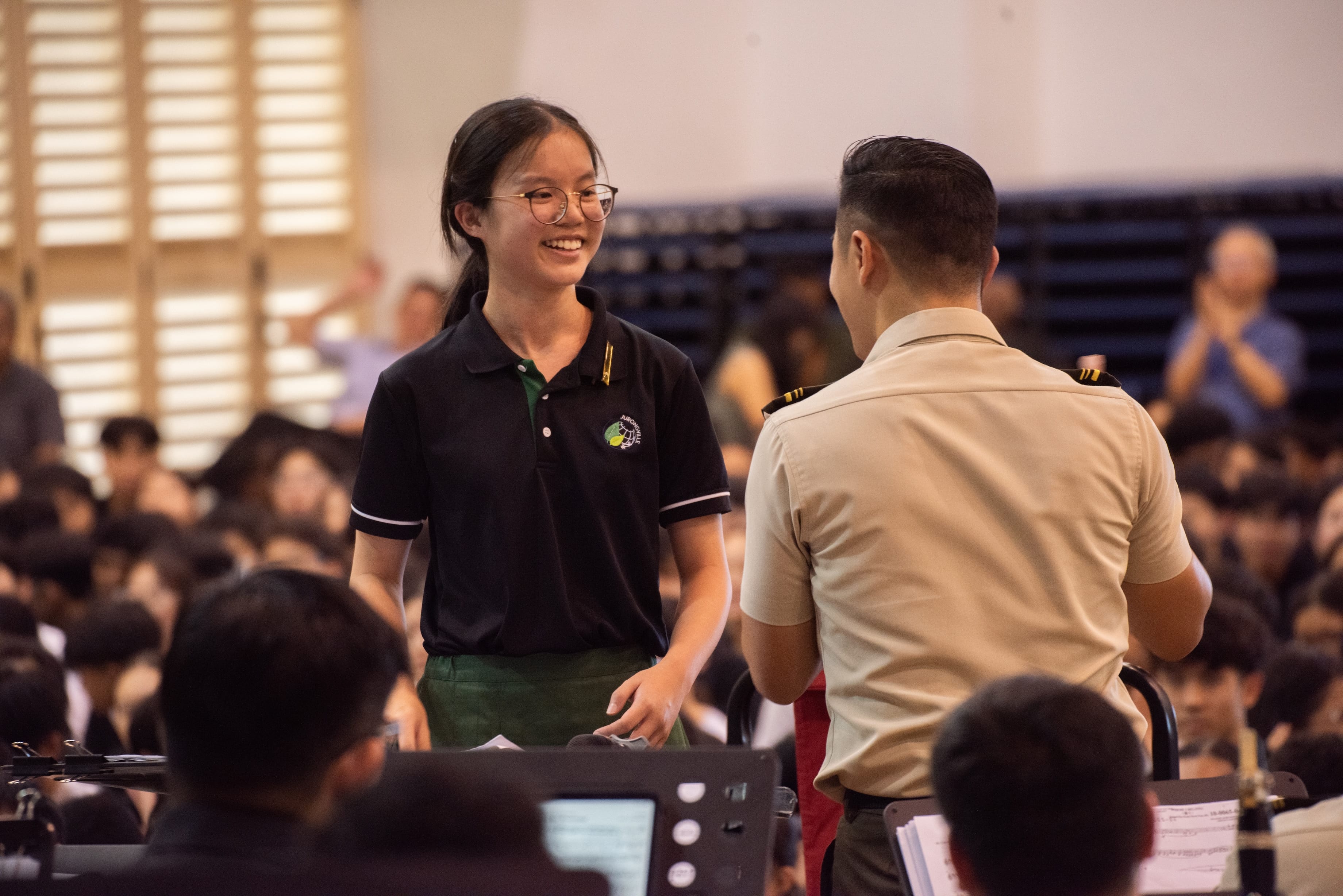 Student smiling while interacting with SAF personnel during a school assembly event.