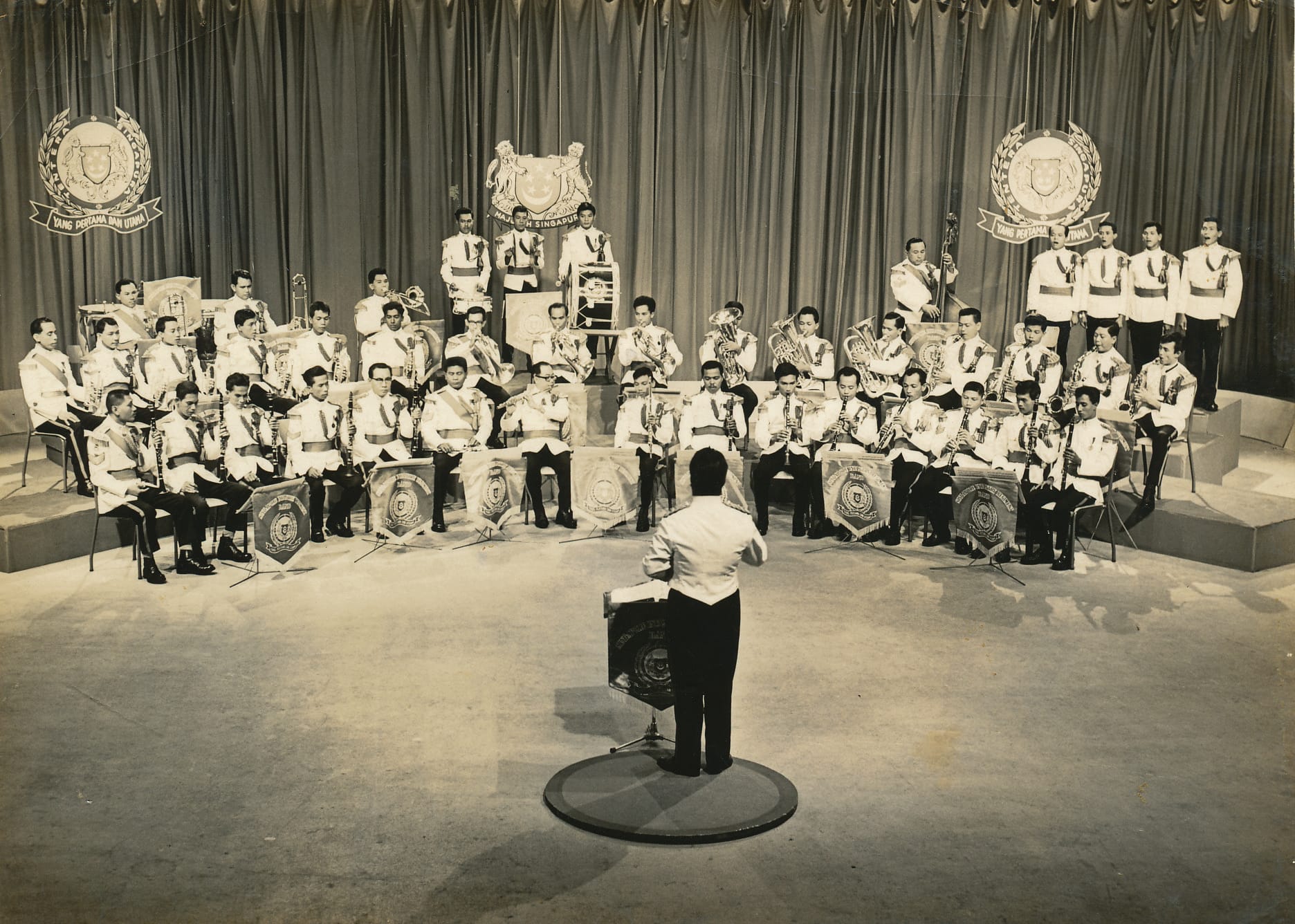 SAF Central Band in ceremonial uniform performing under a conductor in a studio setup.