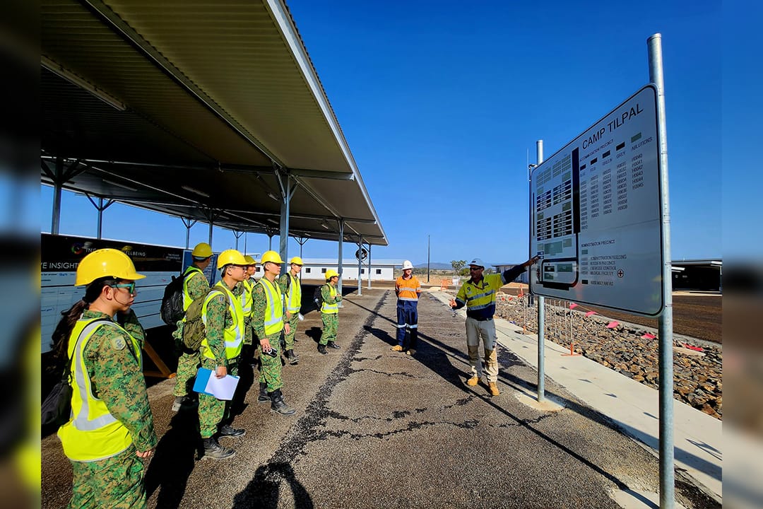 Soldiers in safety gear getting briefed at a construction site signboard.