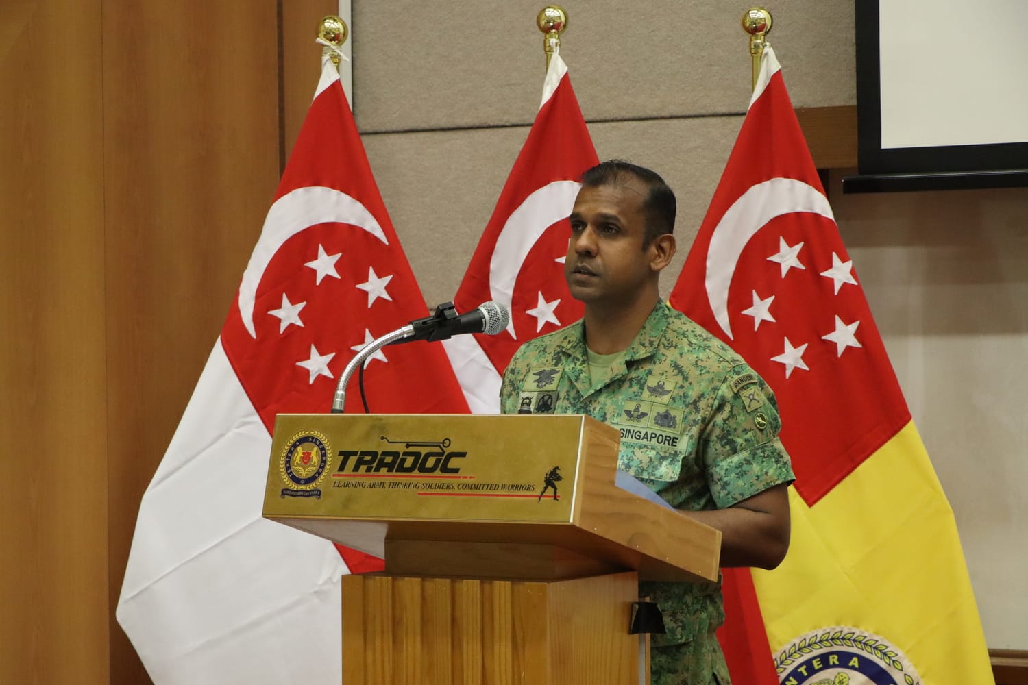 CWO Maheswaran delivering a speech at TRADOC with flags behind him.