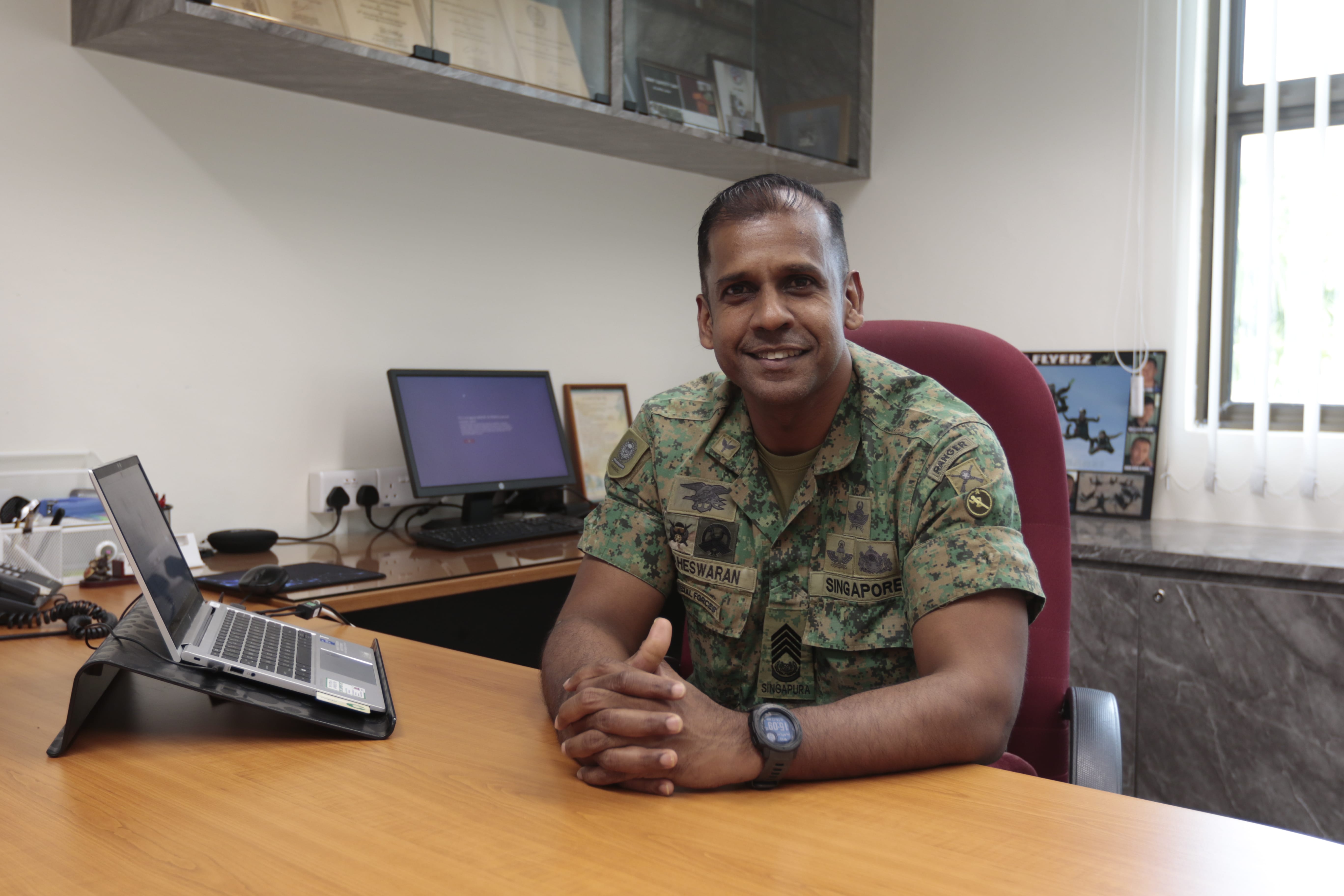 CWO Maheswaran seated at his desk in uniform, smiling in his office.