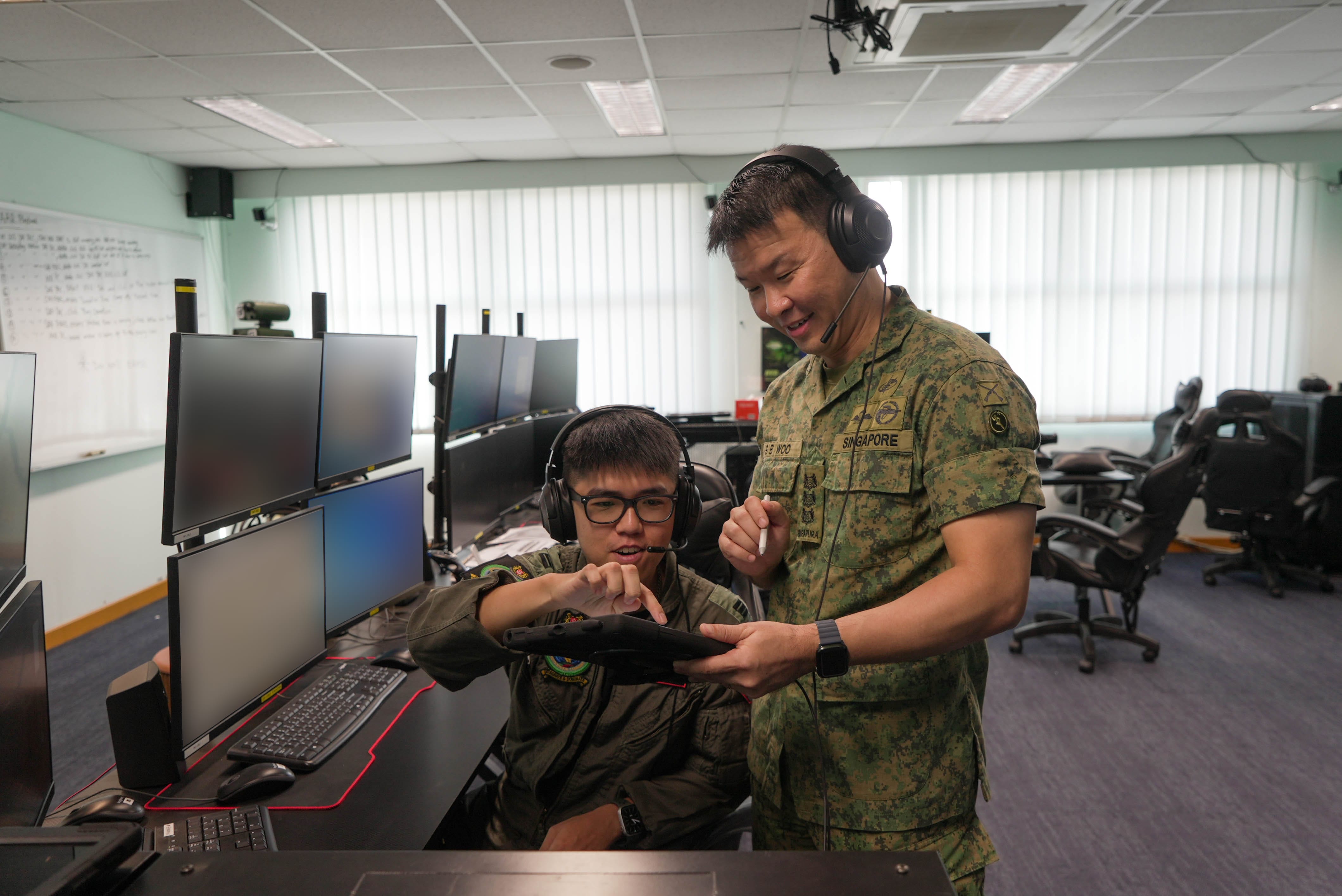 COL Woo advising a trainee in a simulation room with headsets and monitors.