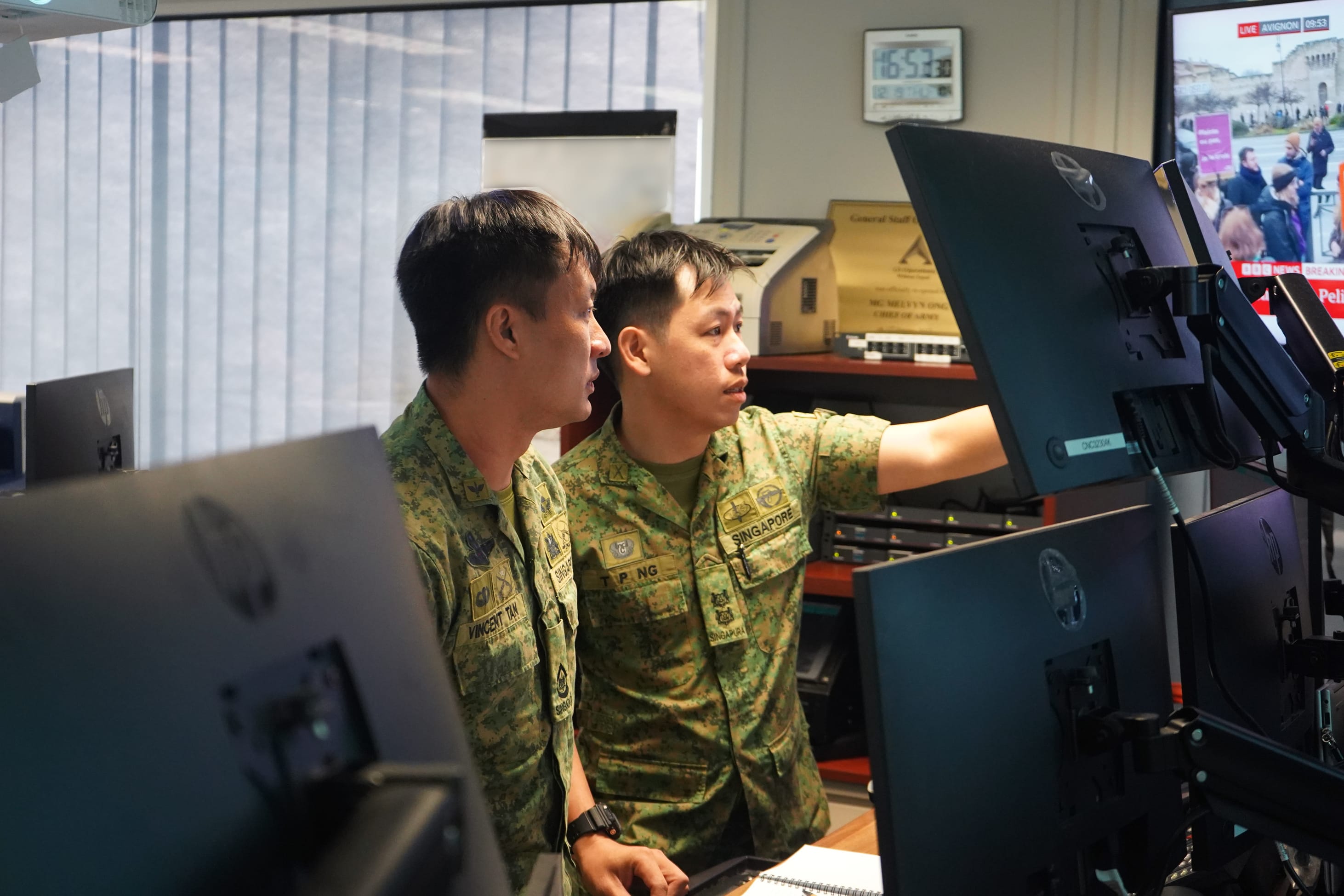 LTC Ng Tze Peng and a fellow officer reviewing data on screens in an ops room.