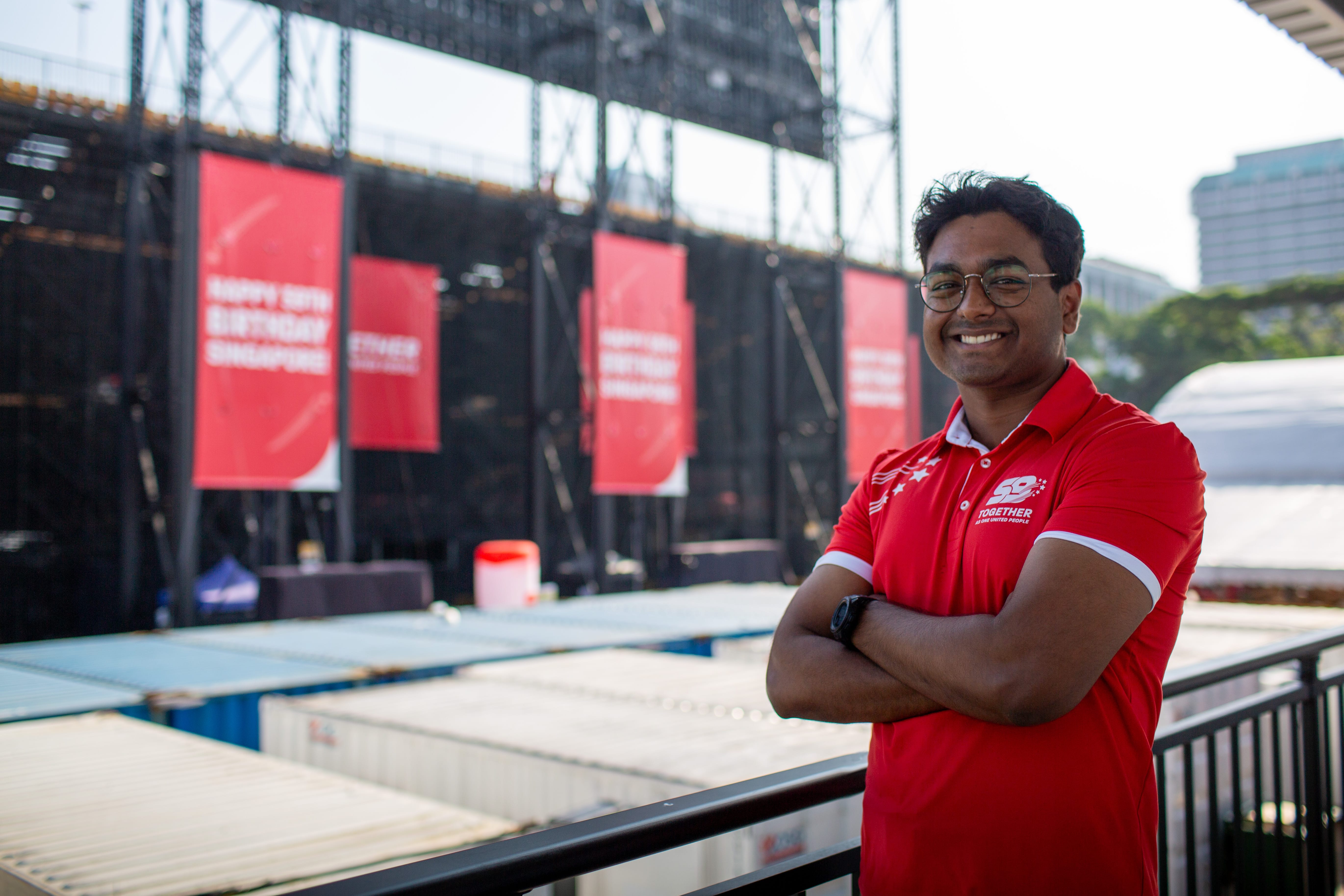 Operations staff in red polo smiling in front of NDP stage and signage.