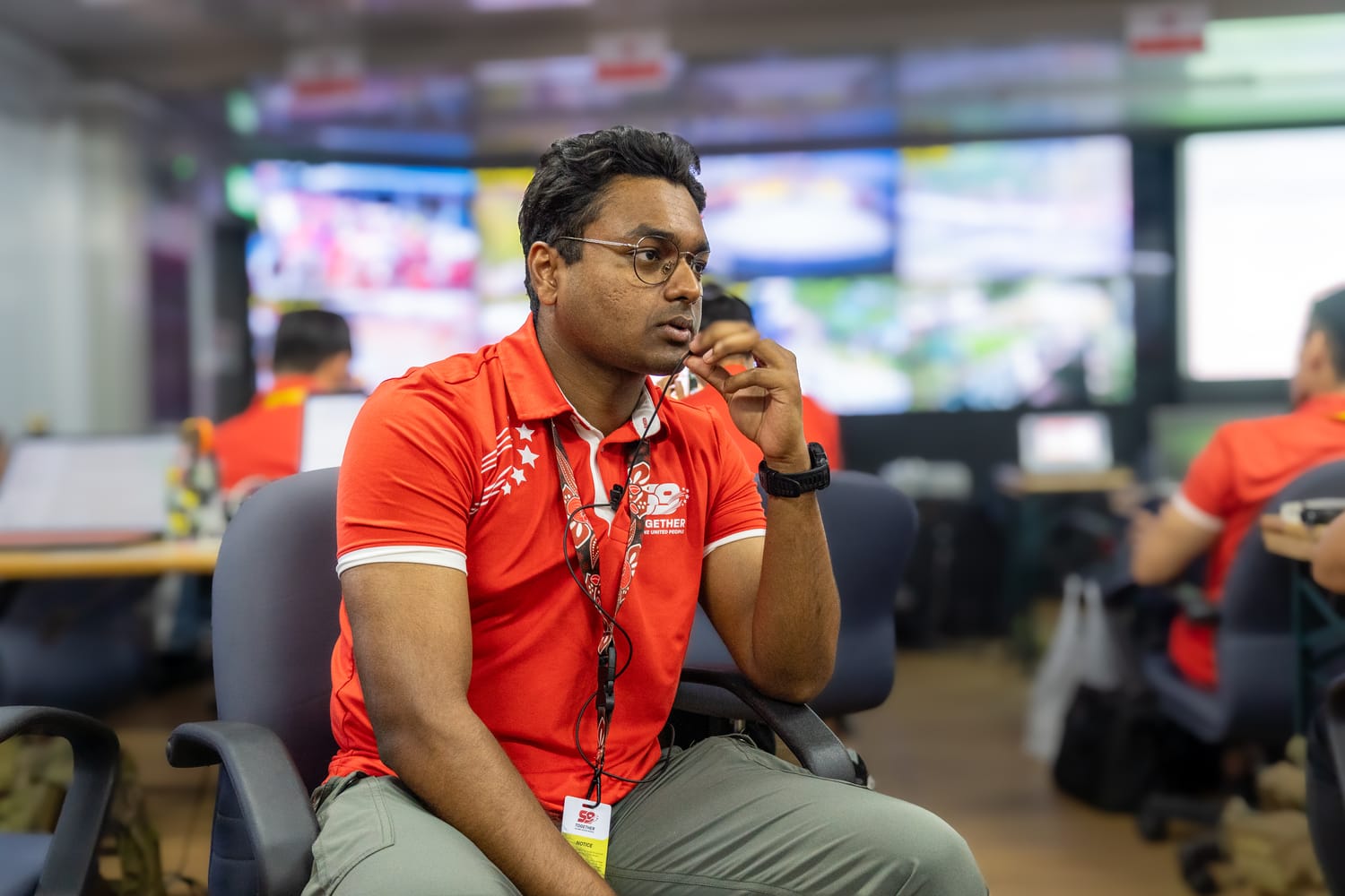 Staff in red polo using walkie-talkie in NDP security control room.