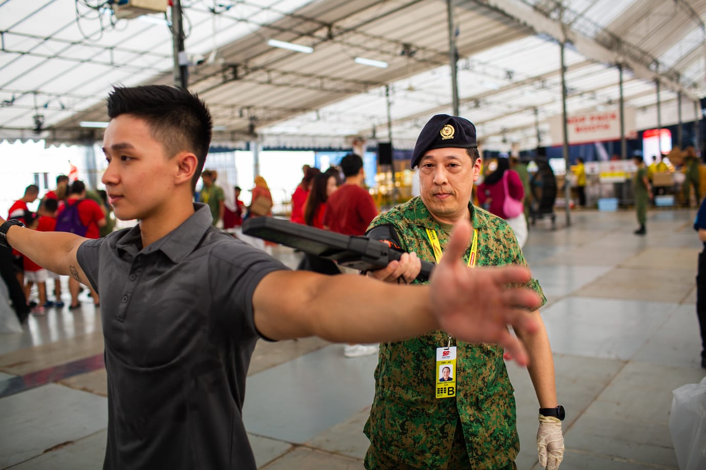 Officer in uniform conducting handheld scanner check at NDP security screening zone.