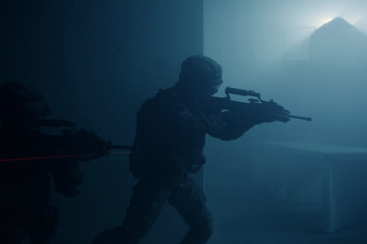 Soldiers with rifles and laser sights move cautiously through a dark, smoke-filled room.