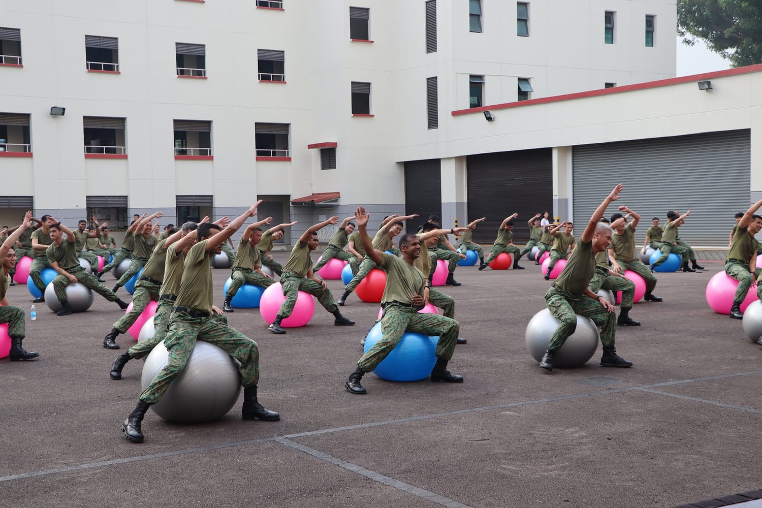 Soldiers doing group exercises on fitness balls in camp courtyard.
