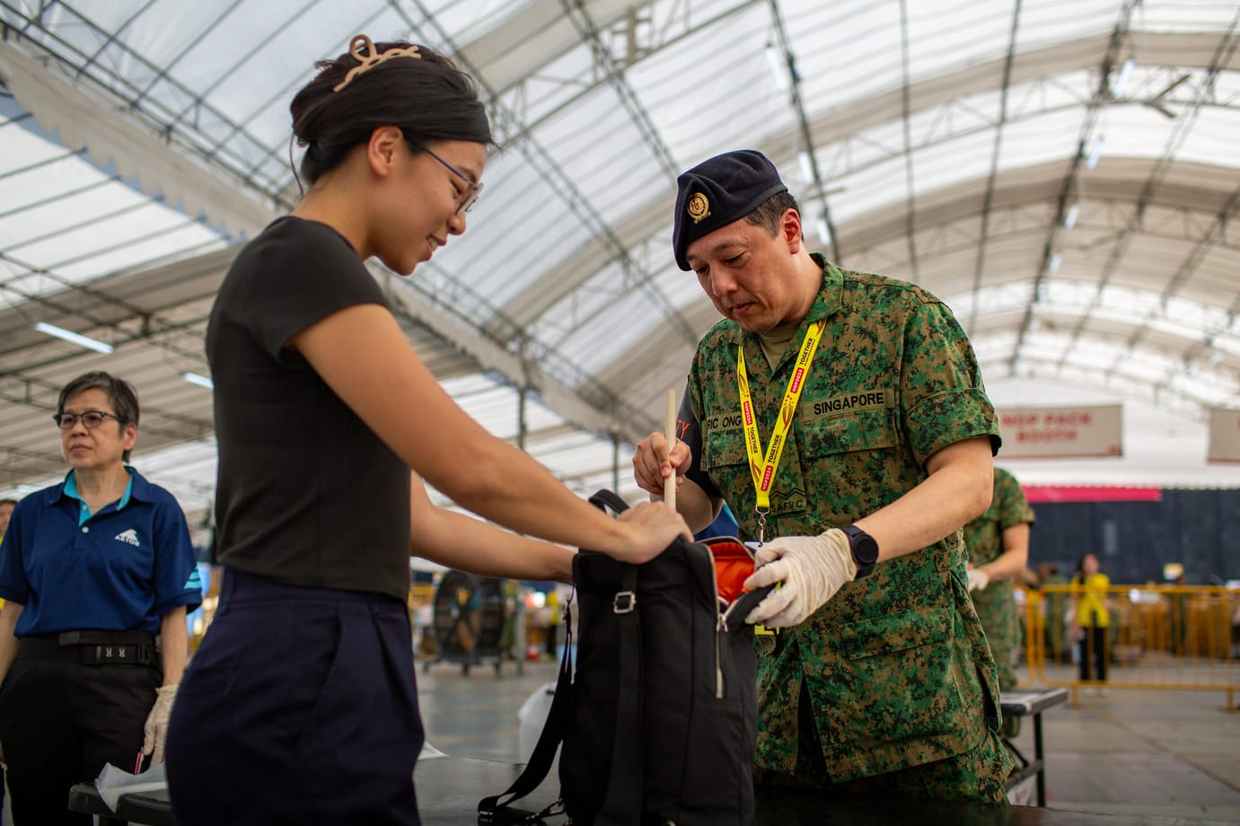 Officer inspecting a backpack during NDP bag check at entrance screening area.