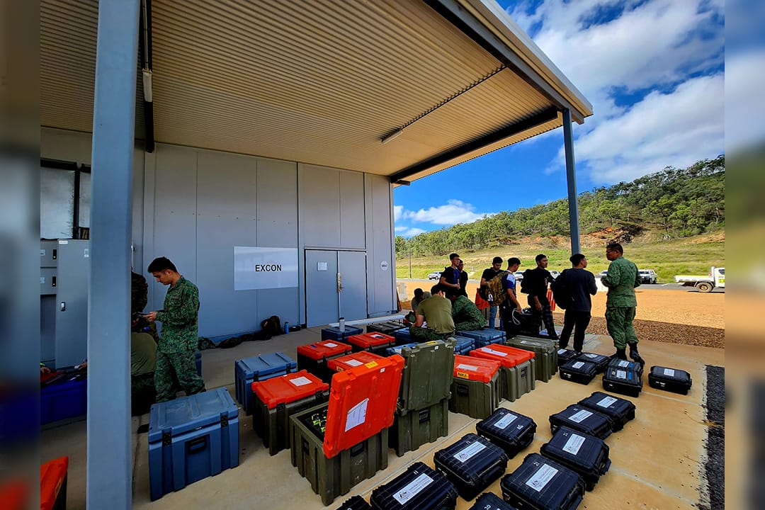 Soldiers sorting equipment outside a building marked EXCON at camp.