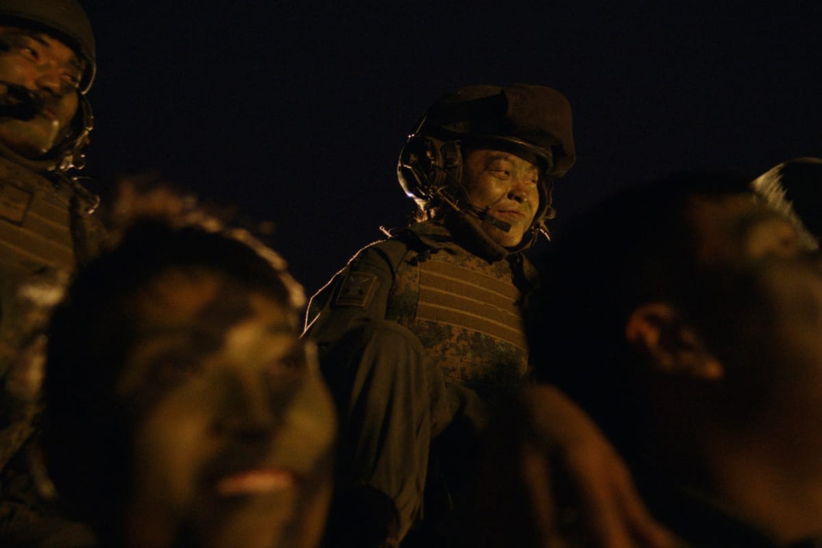 Camouflaged soldier smiling at night while lifted during a team celebration.