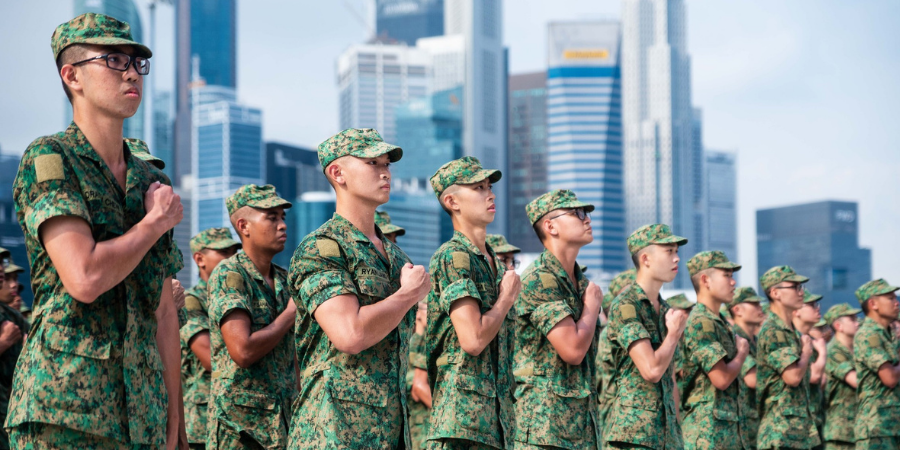 Soldiers standing in formation, saluting with Singapore's city skyline in the background.