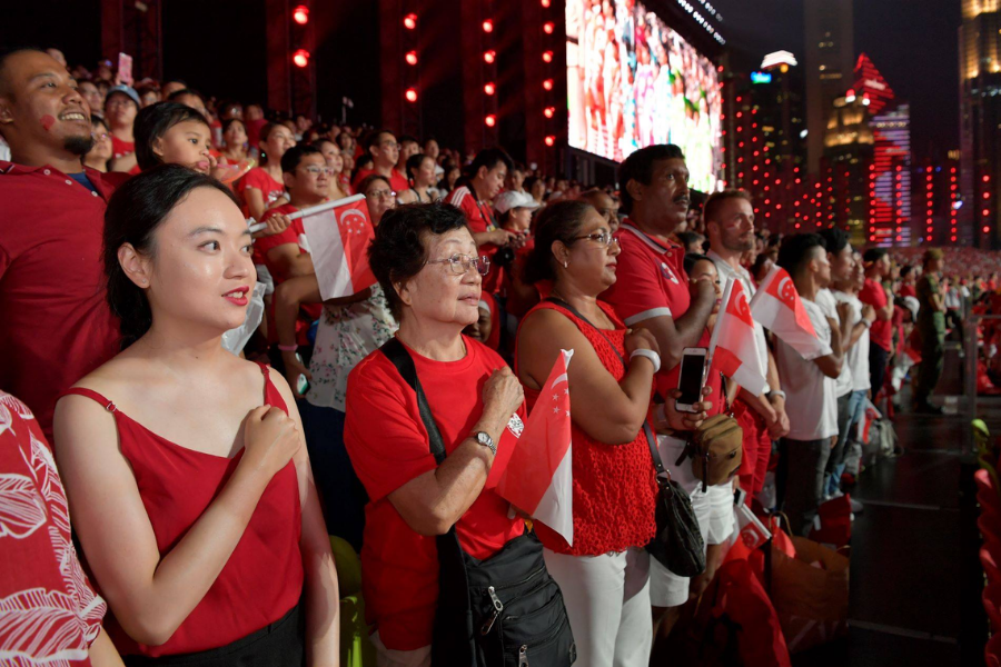 Citizens attending a National Day event, pledging allegiance with Singapore flags.