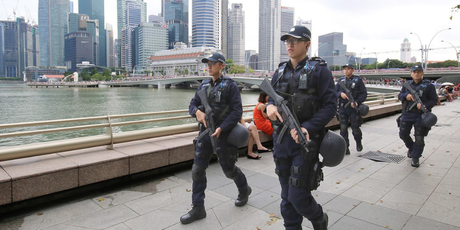 Police officers in tactical gear walking near the Marina Bay waterfront in Singapore.