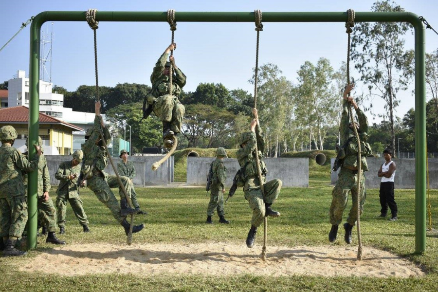 Soldiers climbing ropes during physical training at a military camp.