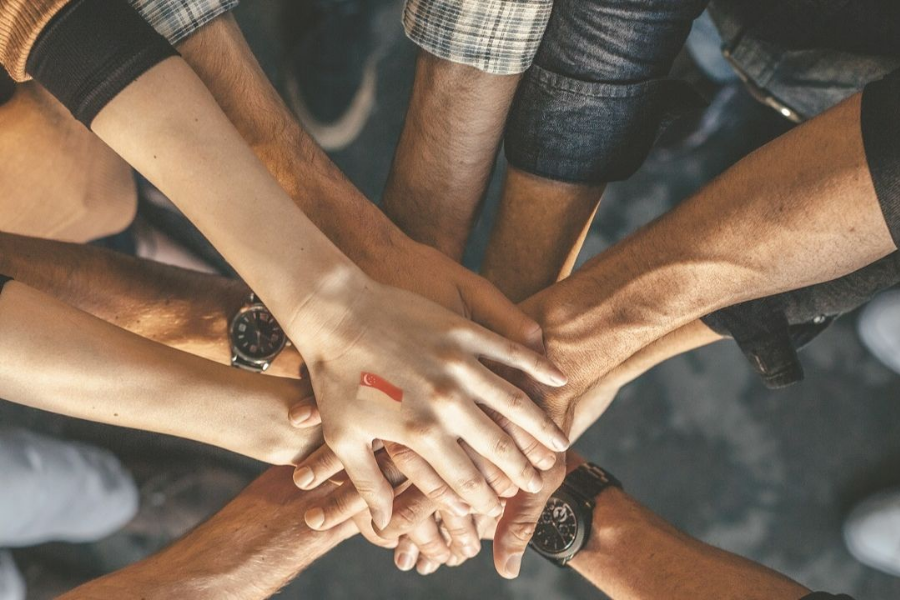 Close-up of diverse hands joining together with a Singapore flag tattoo symbolizing unity.