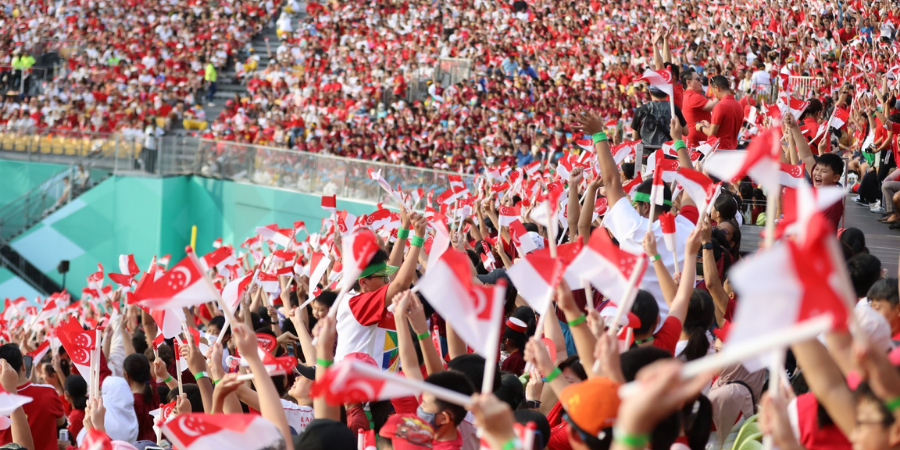 Crowd of Singaporeans waving flags, celebrating National Day with spirited pride.