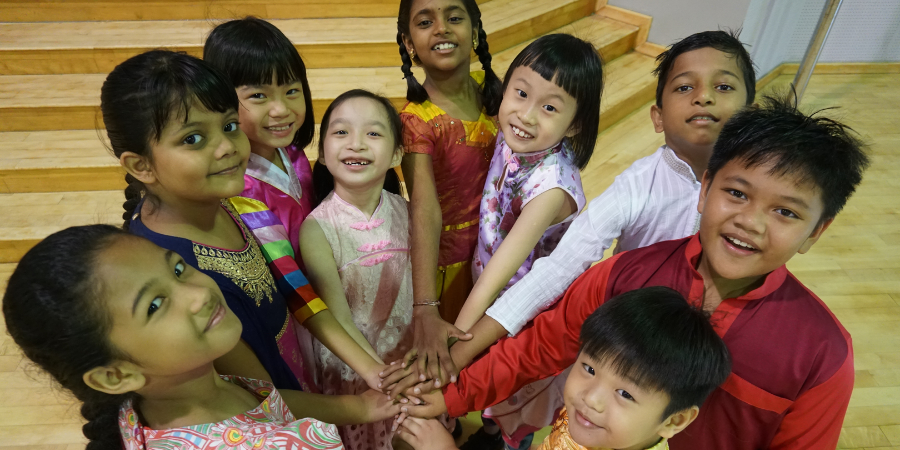 A group of children standing together, smiling and holding hands in a circle.