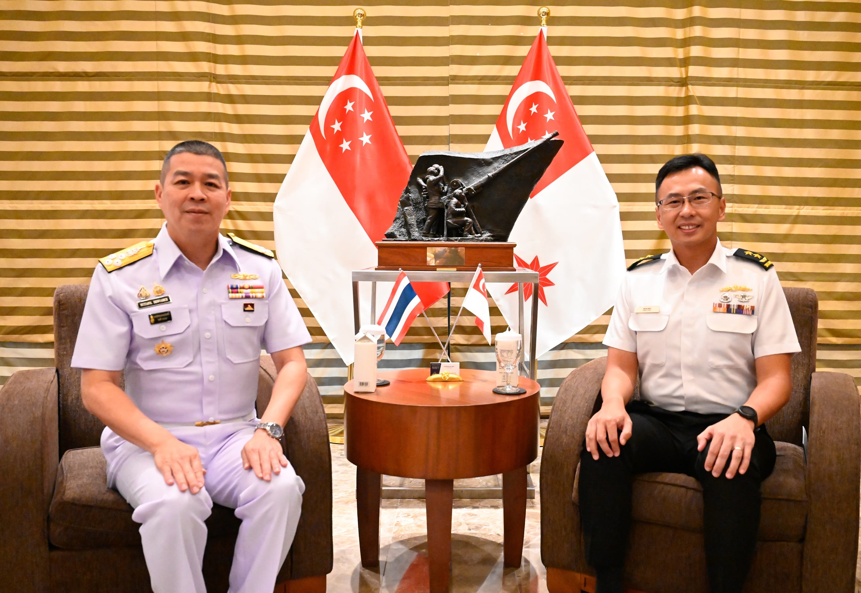 Two uniformed officers seated with Singapore flags and a sculpture in the background.