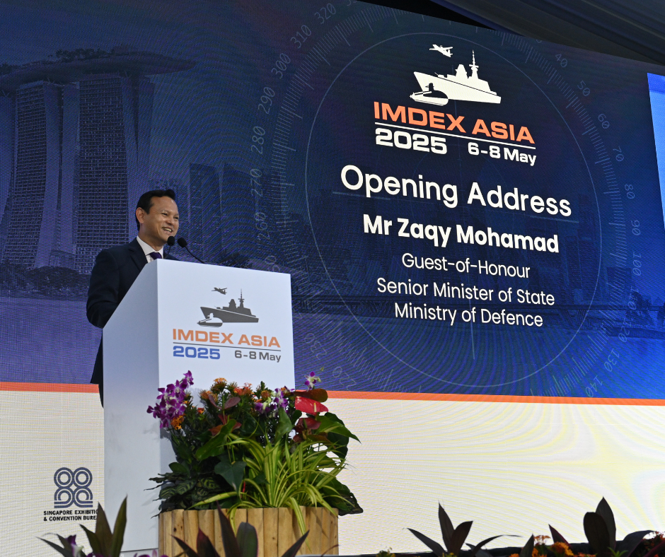 Man at IMDEX ASIA 2025 opening address, podium with logo, floral arrangement.