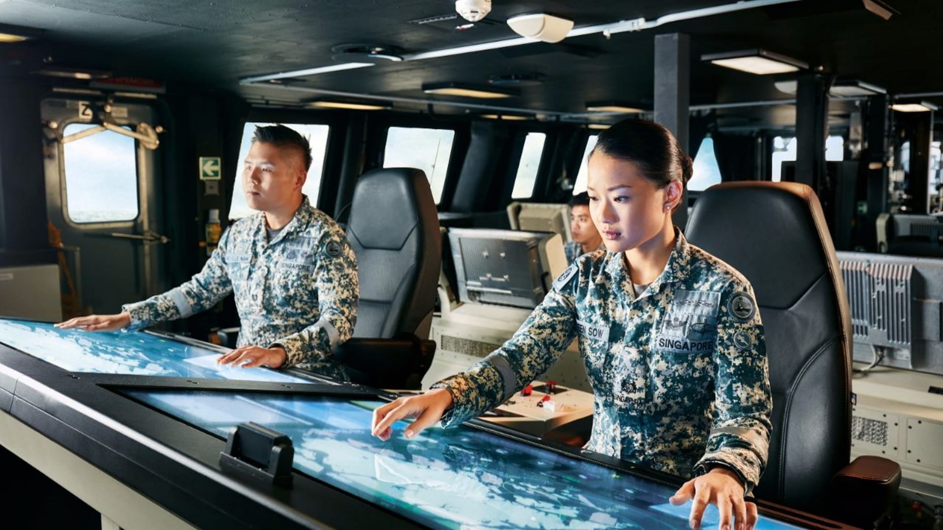 MAJ Eileen Sow and crew operate touch-screen navigation systems on a naval ship’s bridge.