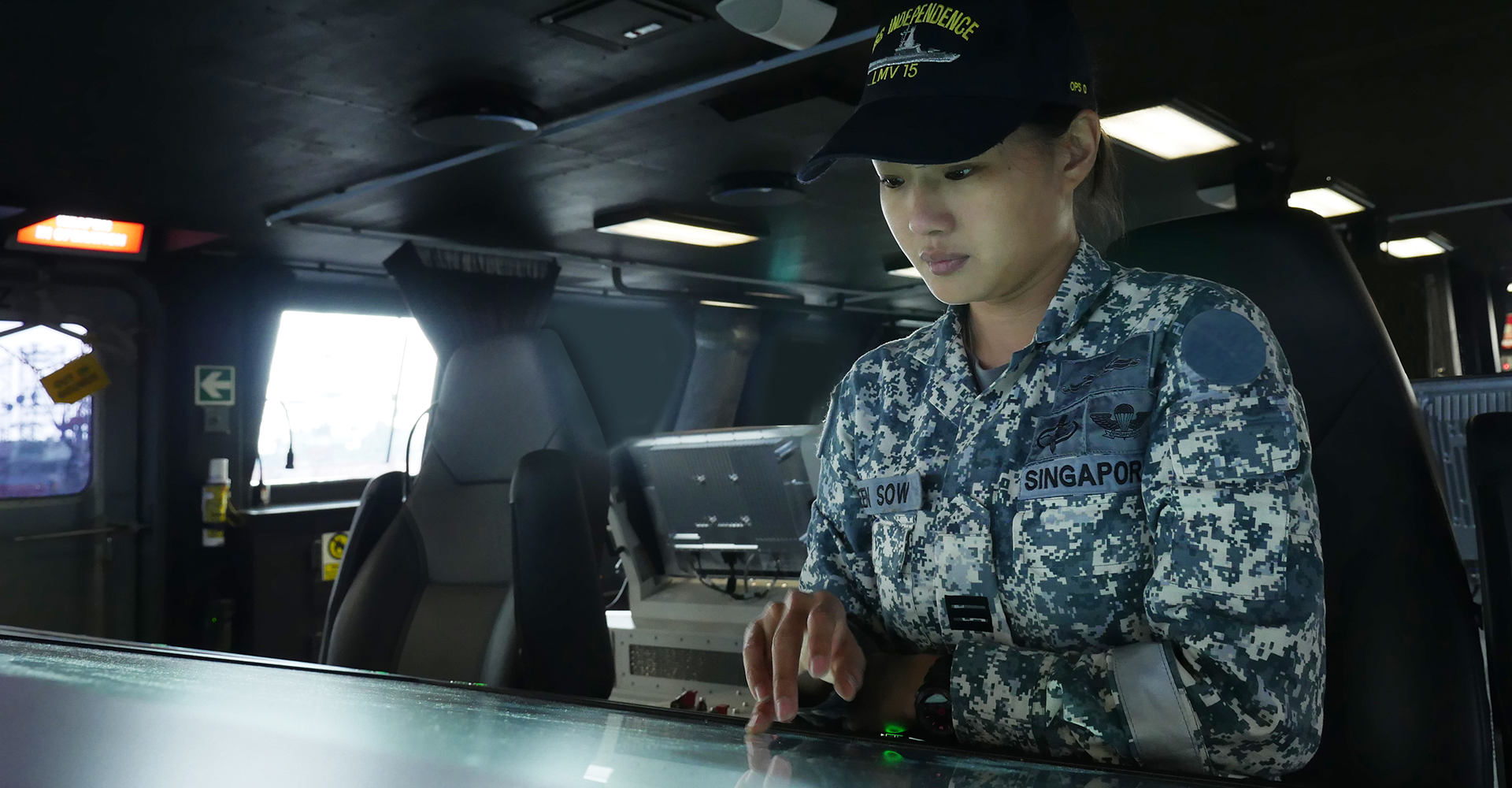 Navy specialist using a touchscreen control panel inside a ship's bridge.