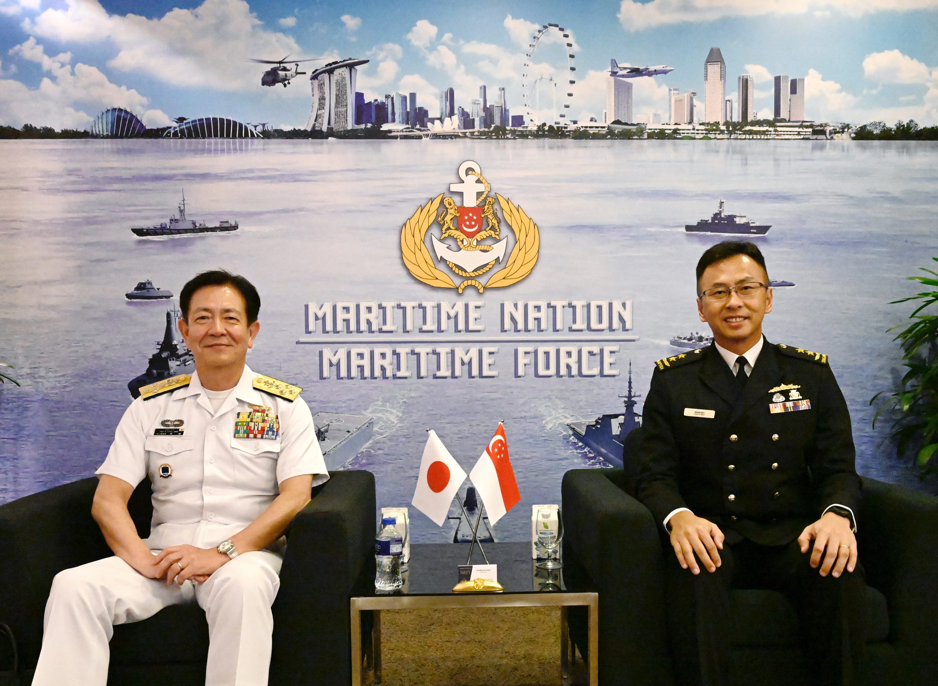 Two naval officers seated, with flags of Japan and Singapore in front, backdrop of Maritime Nation Maritime Force.