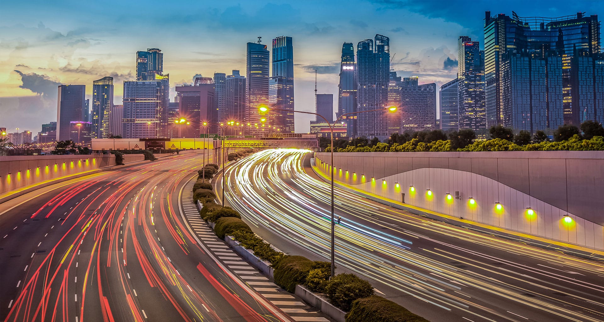 Light trails from vehicles on a highway with Singapore city skyline at dusk.