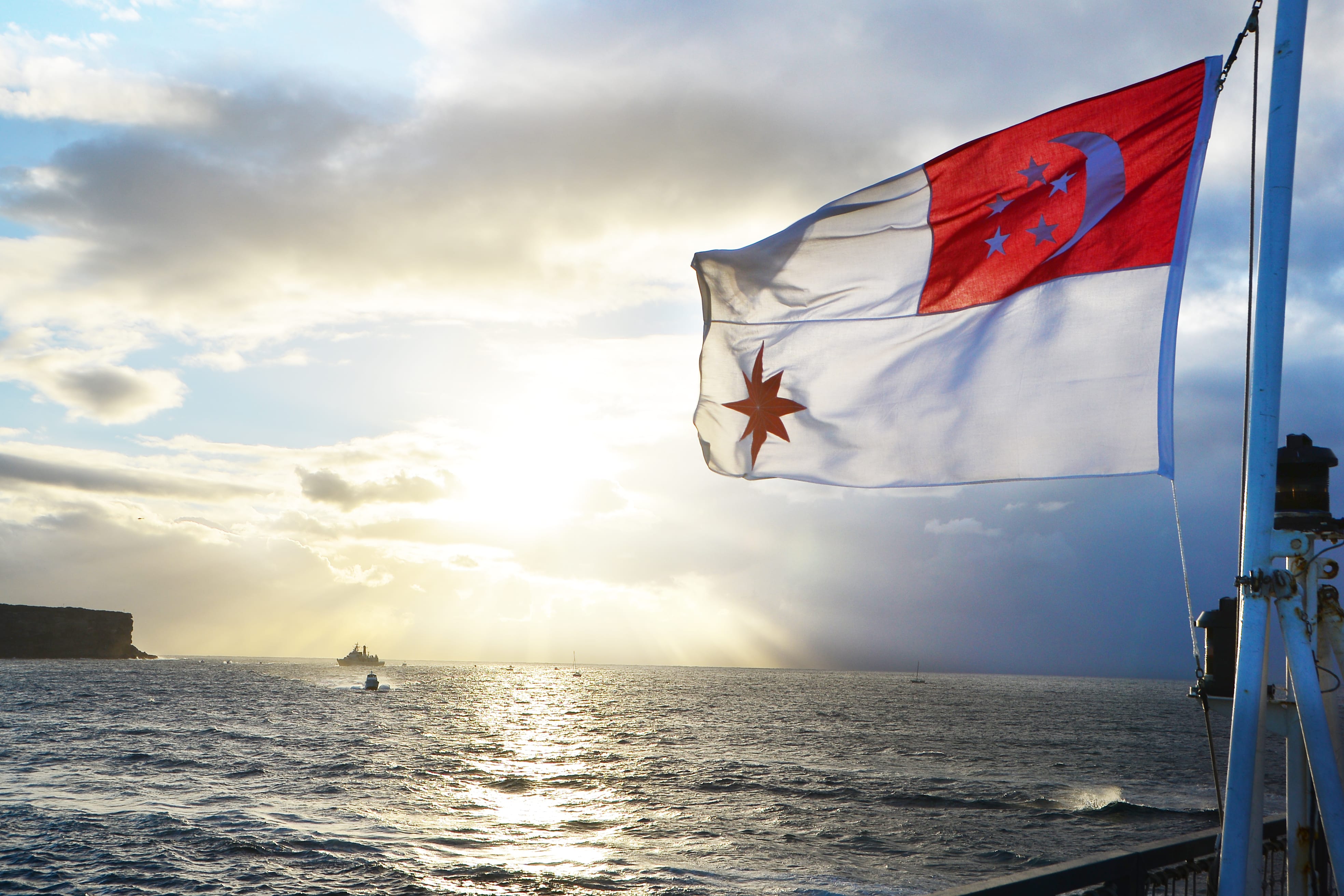 The Singapore flag flying over a Navy vessel with the setting sun in the background.