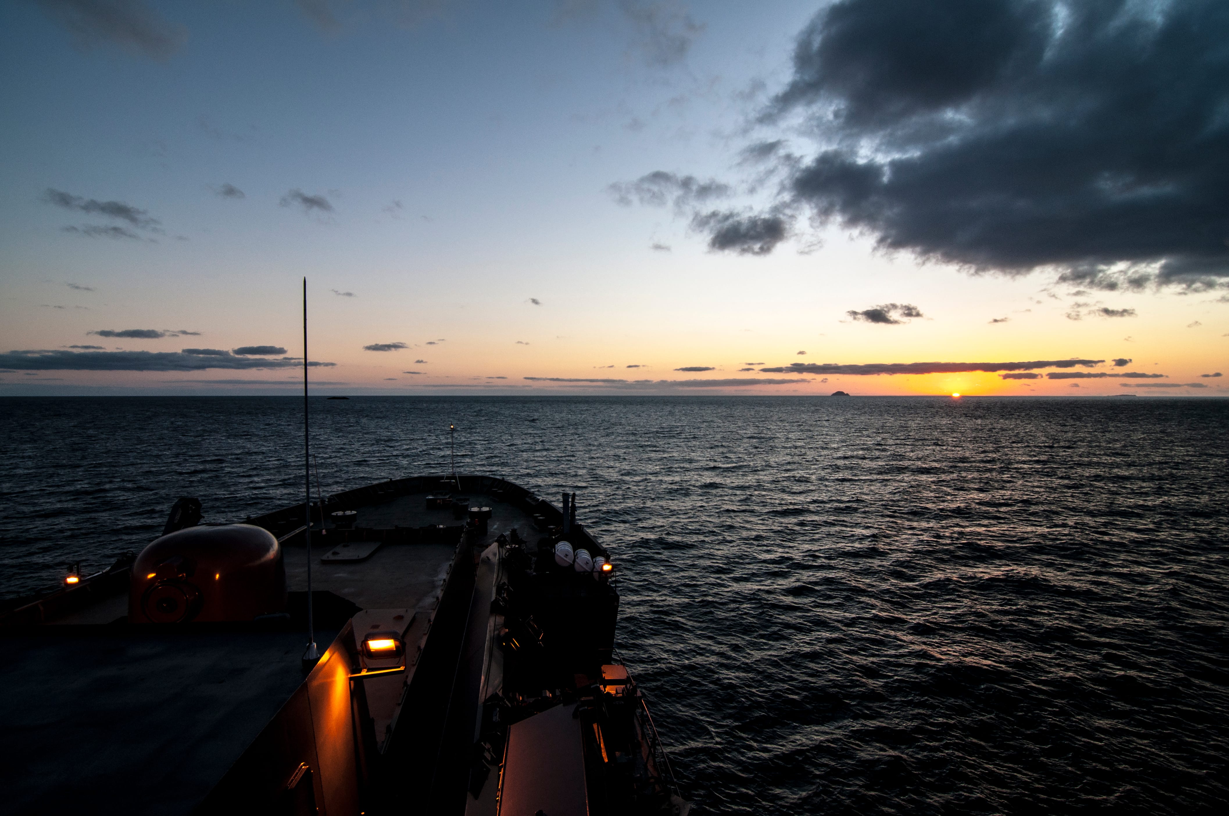 A view from a ship's bridge as the sun sets over the ocean.