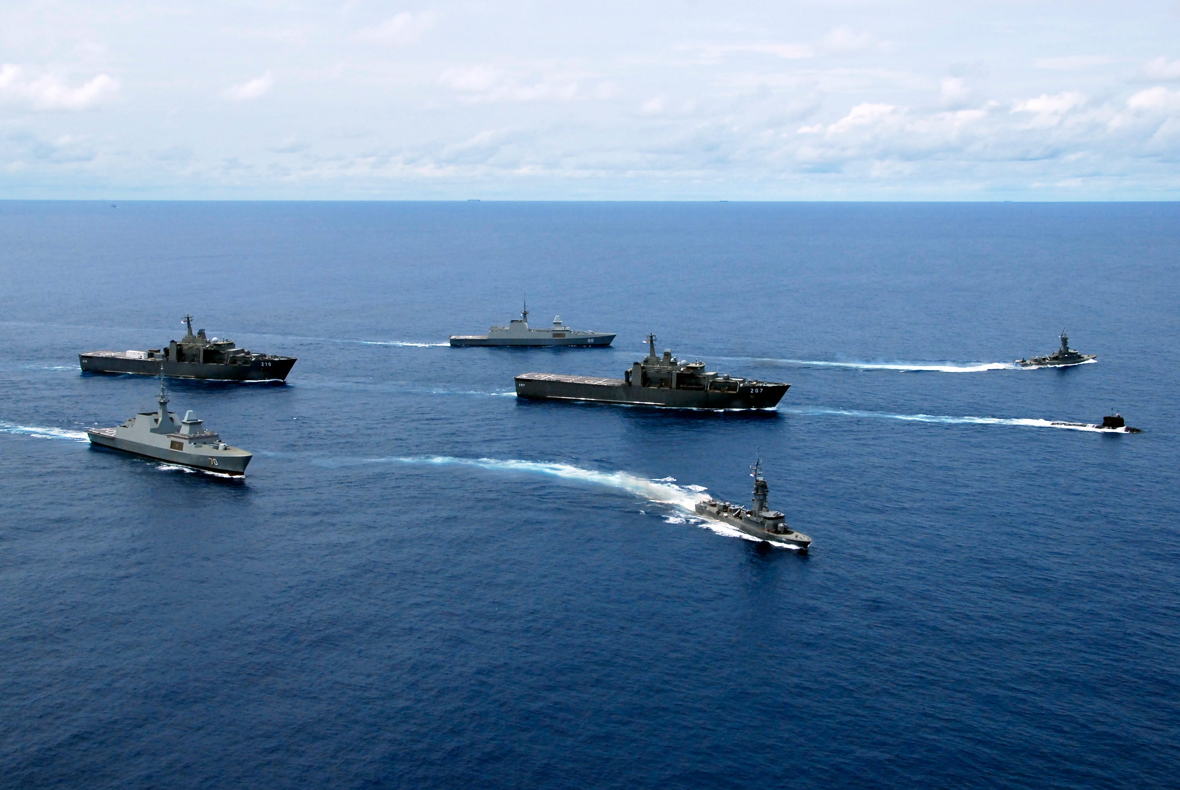 Multiple navy vessels, including frigates and support ships, maneuver in formation across the sea.