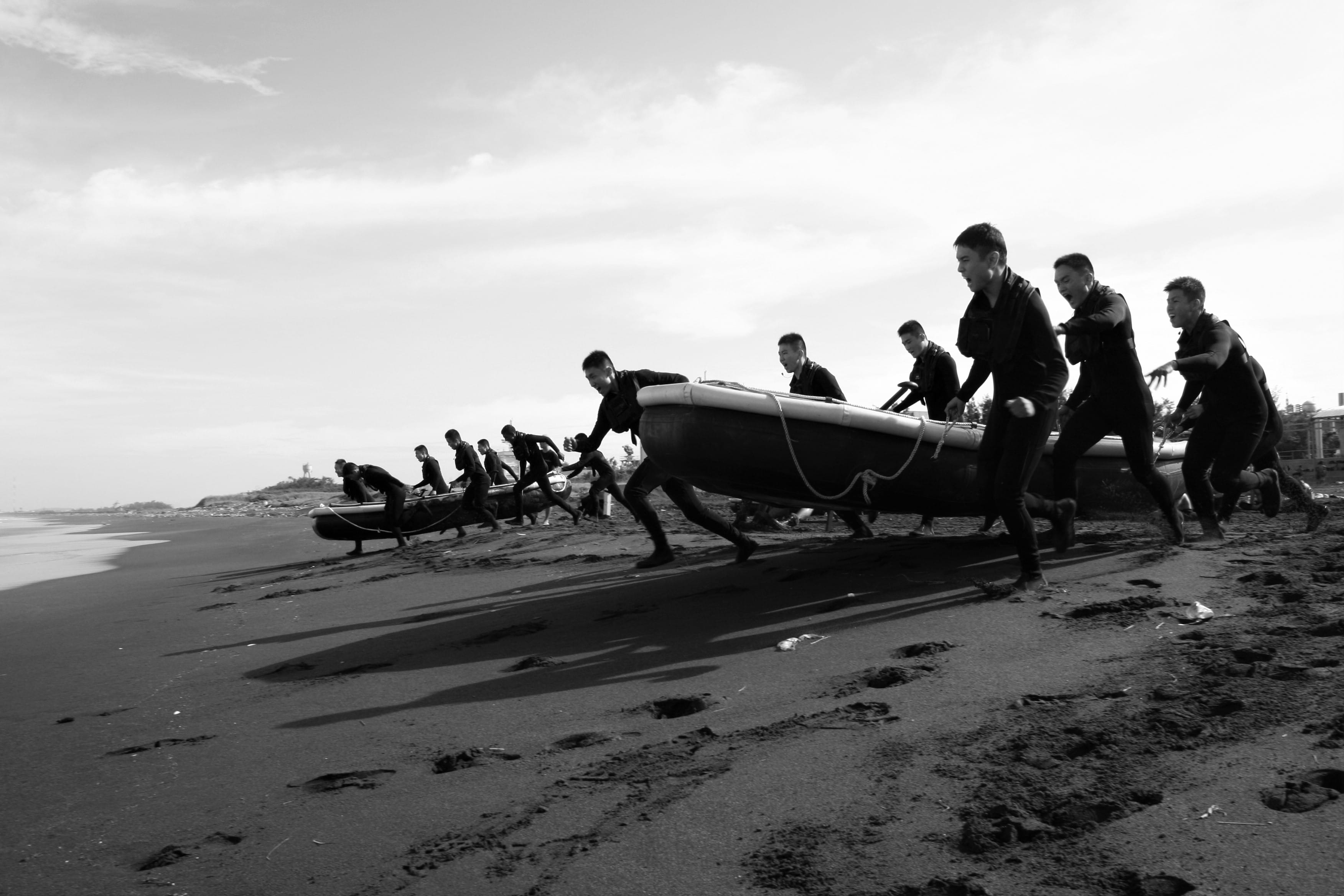 Military personnel hauling a rubber boat along the beach as part of their training.