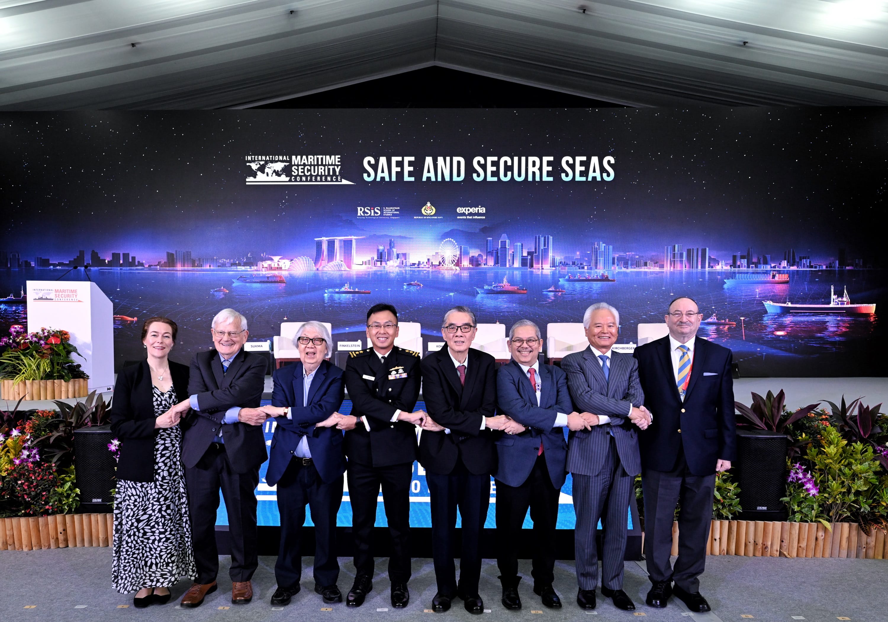 Panellists link arms on stage under the "Safe and Secure Seas" banner at the IMSC 2025.
