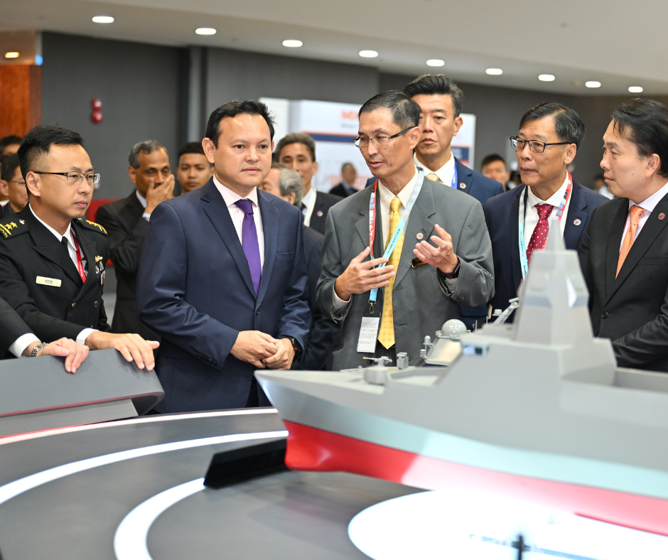 Group of men in suits and military uniform examine a model warship.