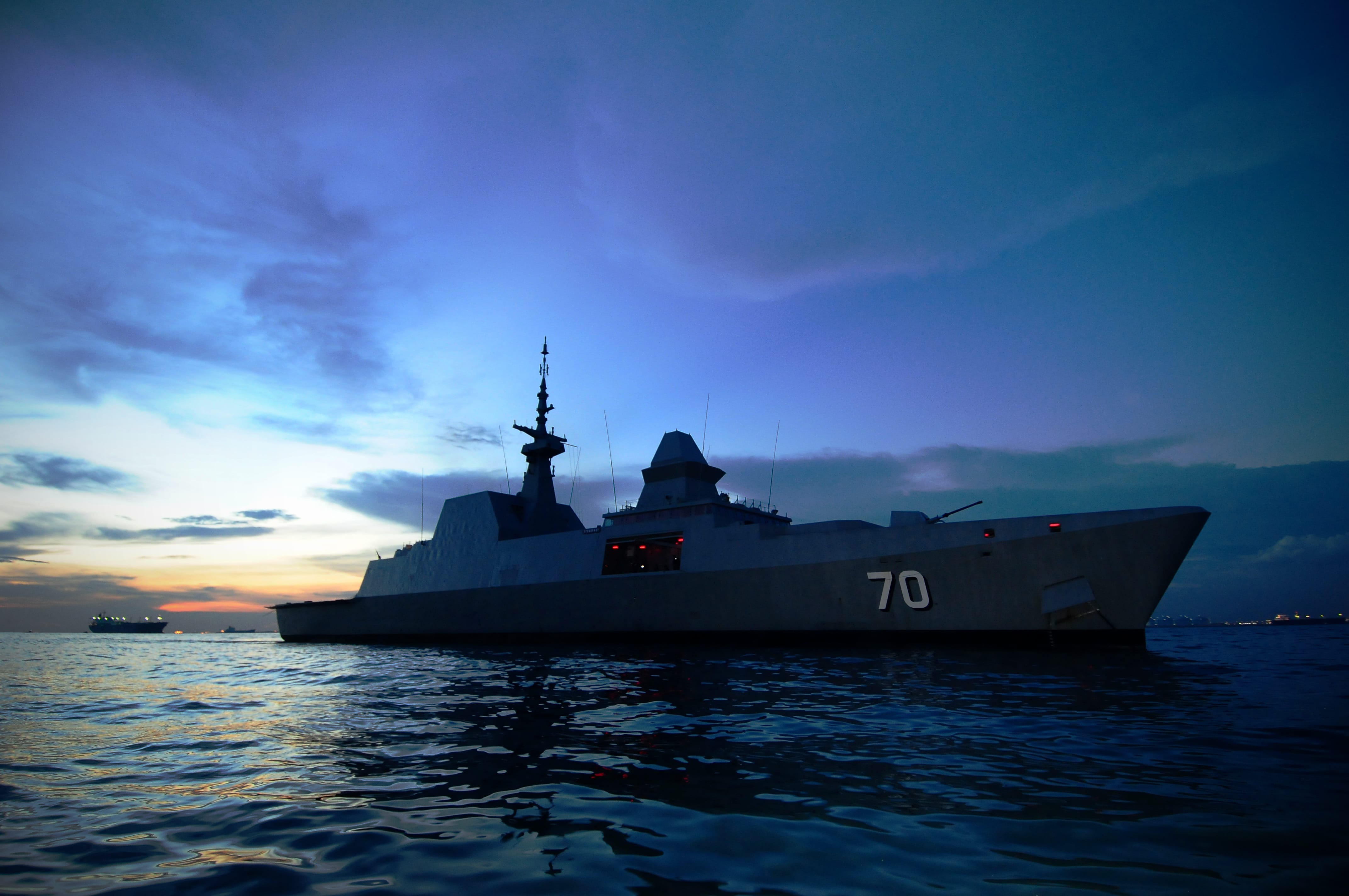 A frigate navigating through the sea with military personnel visible on board.