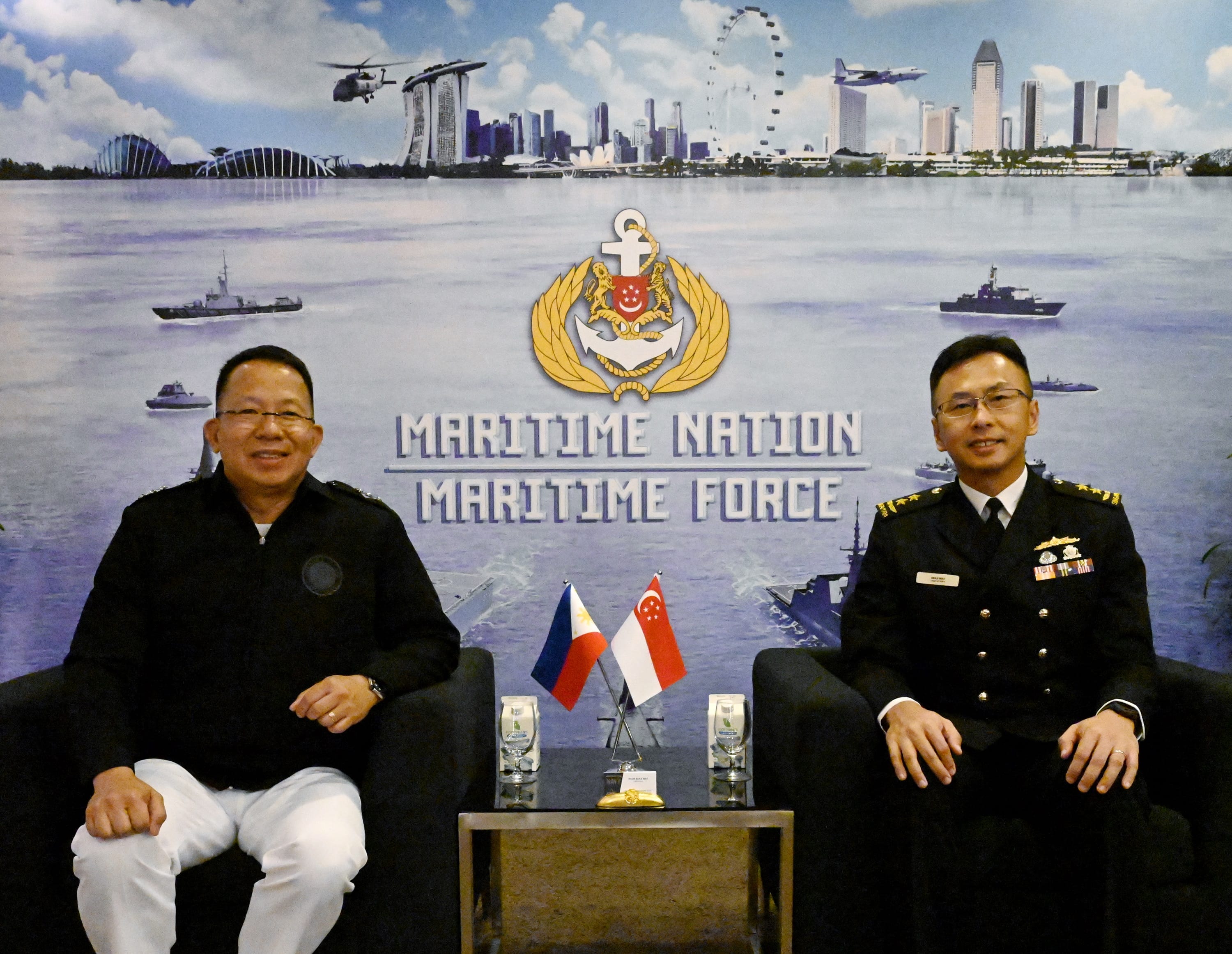 Two naval officers seated, with flags of Philippines and Singapore in front, backdrop of Maritime Nation Maritime Force.