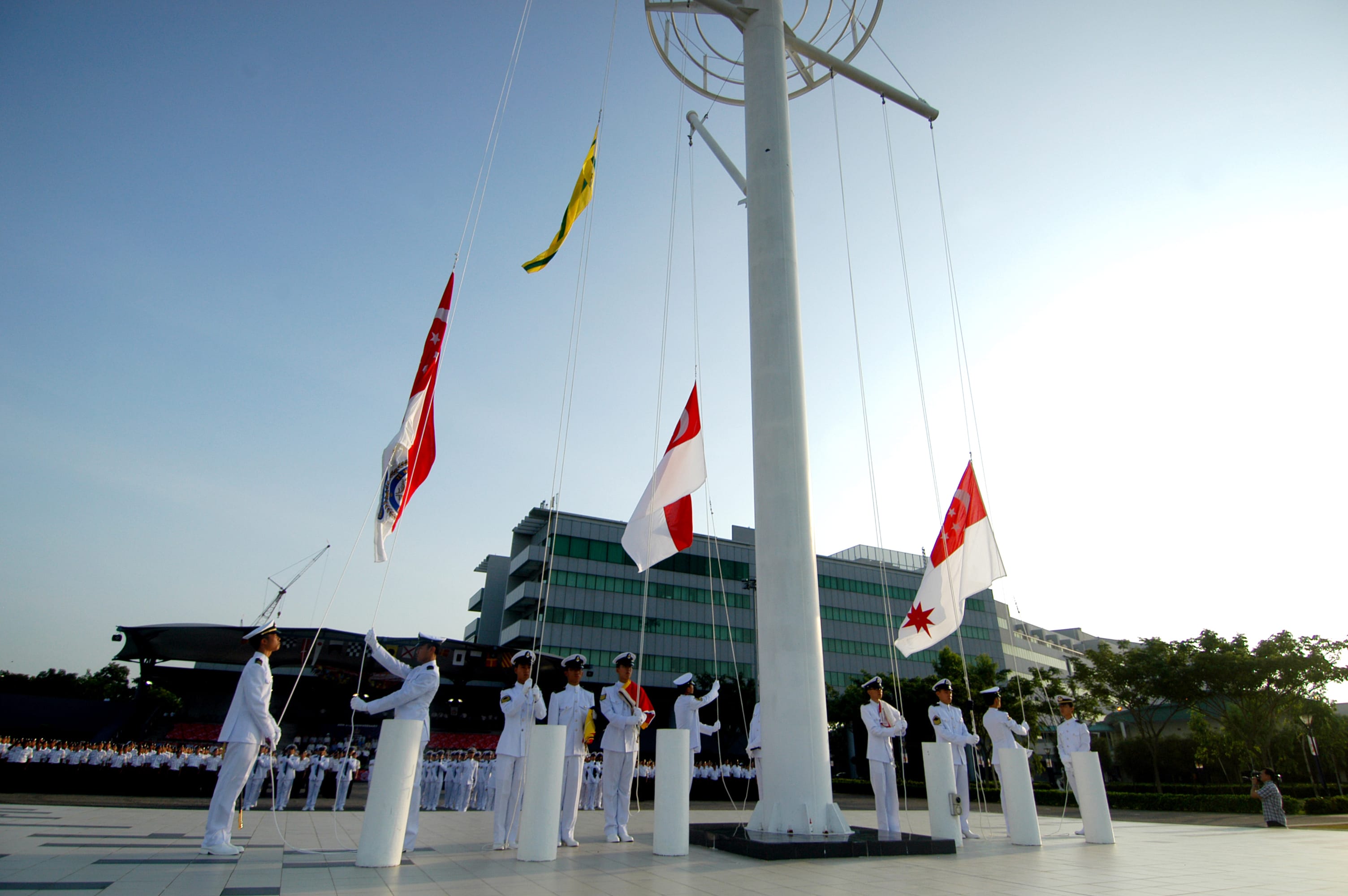 Navy officers raising the Singapore flag during a ceremony on a sunny day.